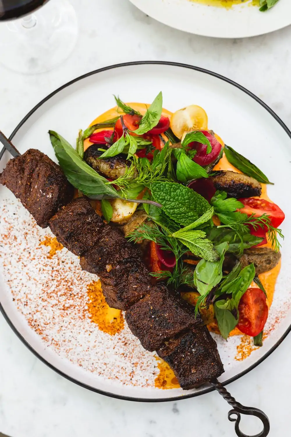 A white plate of grilled lamb skewers served with a colorful vegetable salad and a creamy sauce at Momed, one of the best cozy restaurants in Los Angeles, available on OpenTable.