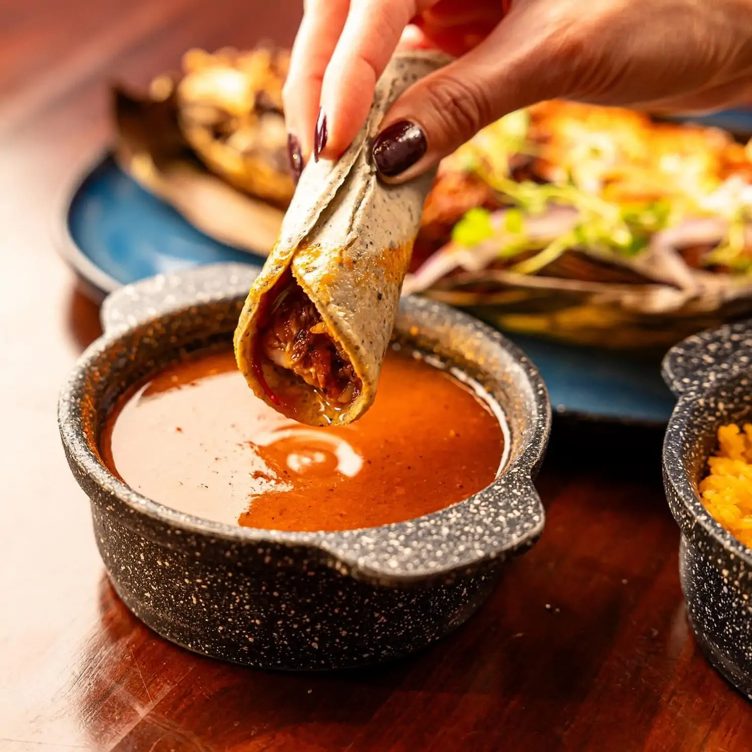 A hand dips a taco into a red dipping sauce at Xalisko Cocina Mexicana, one of the best Mexican restaurants in Houston on OpenTable.