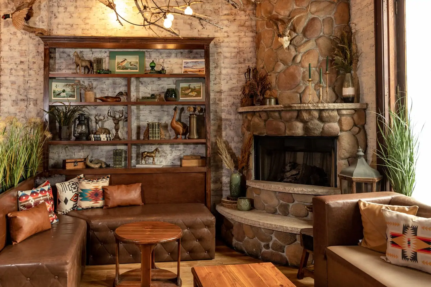 A dining area featuring a stone fireplace in the corner with dark brown leather couches and traditional American hunting decor on the walls at Frontier, one of the best date restaurants in Chicago available on OpenTable.
