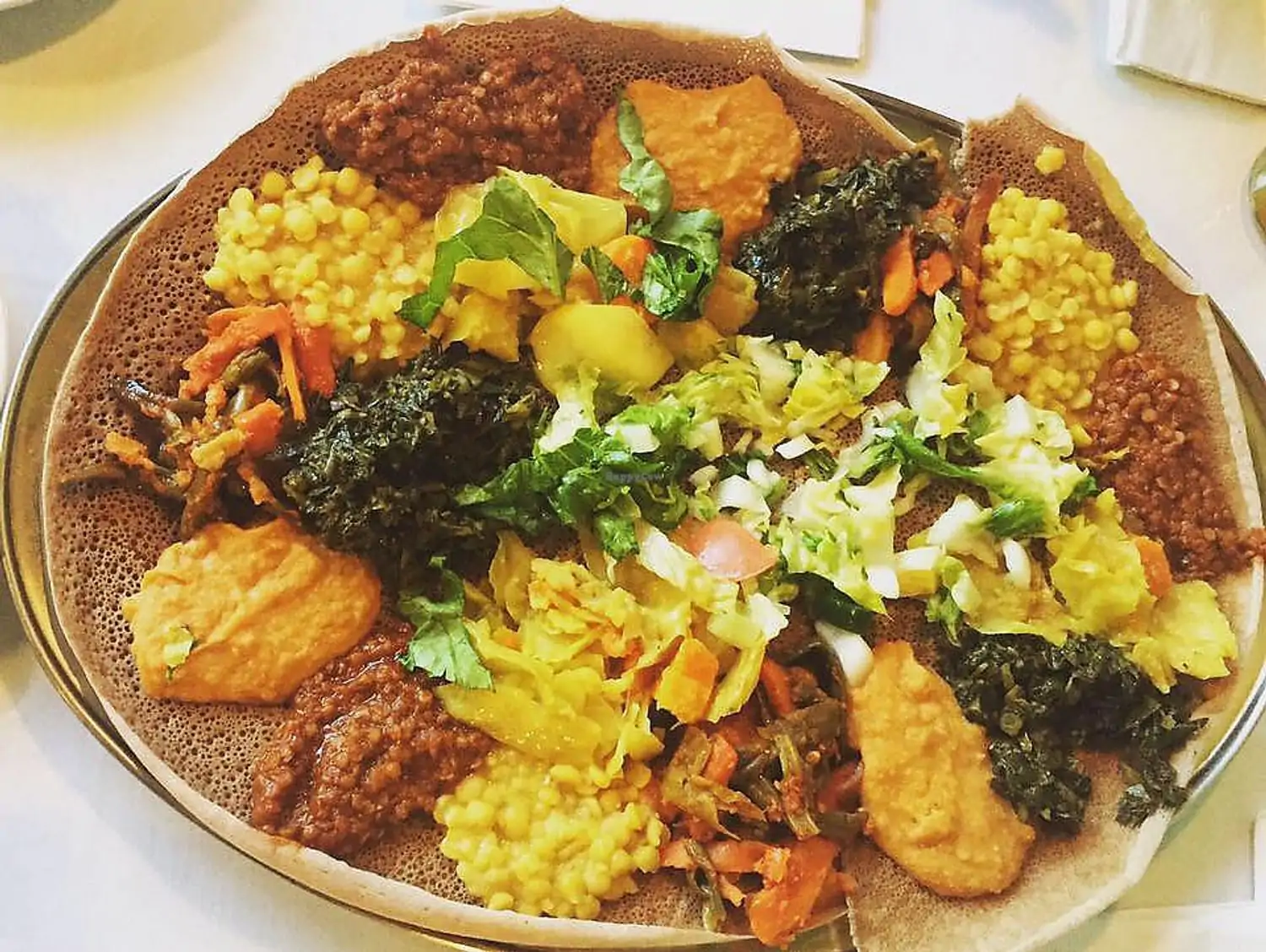 A vegetarian platter at Blue Nile Ethiopian Restaurant, one of the best restaurants in Boston. It is available on OpenTable. The plate includes spiced lentils, cooked vegetables, stews, and salads, all served on traditional injera bread.