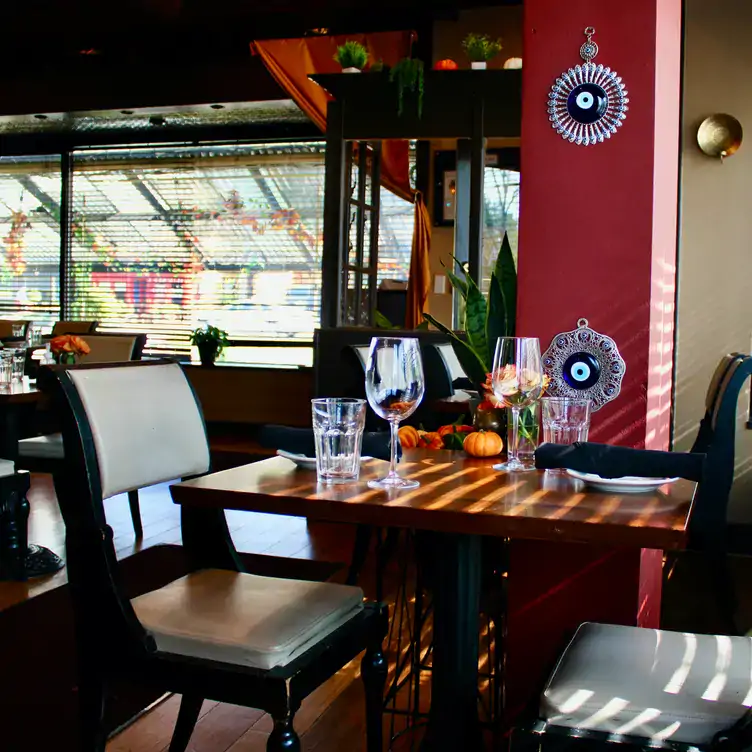 This is a view of the dining room at Bistro Aracosia, one of the best vegetarian restaurants in DC, available on OpenTable. A table for two is set with wine glasses and black napkins. The walls are red with evil eye accents.