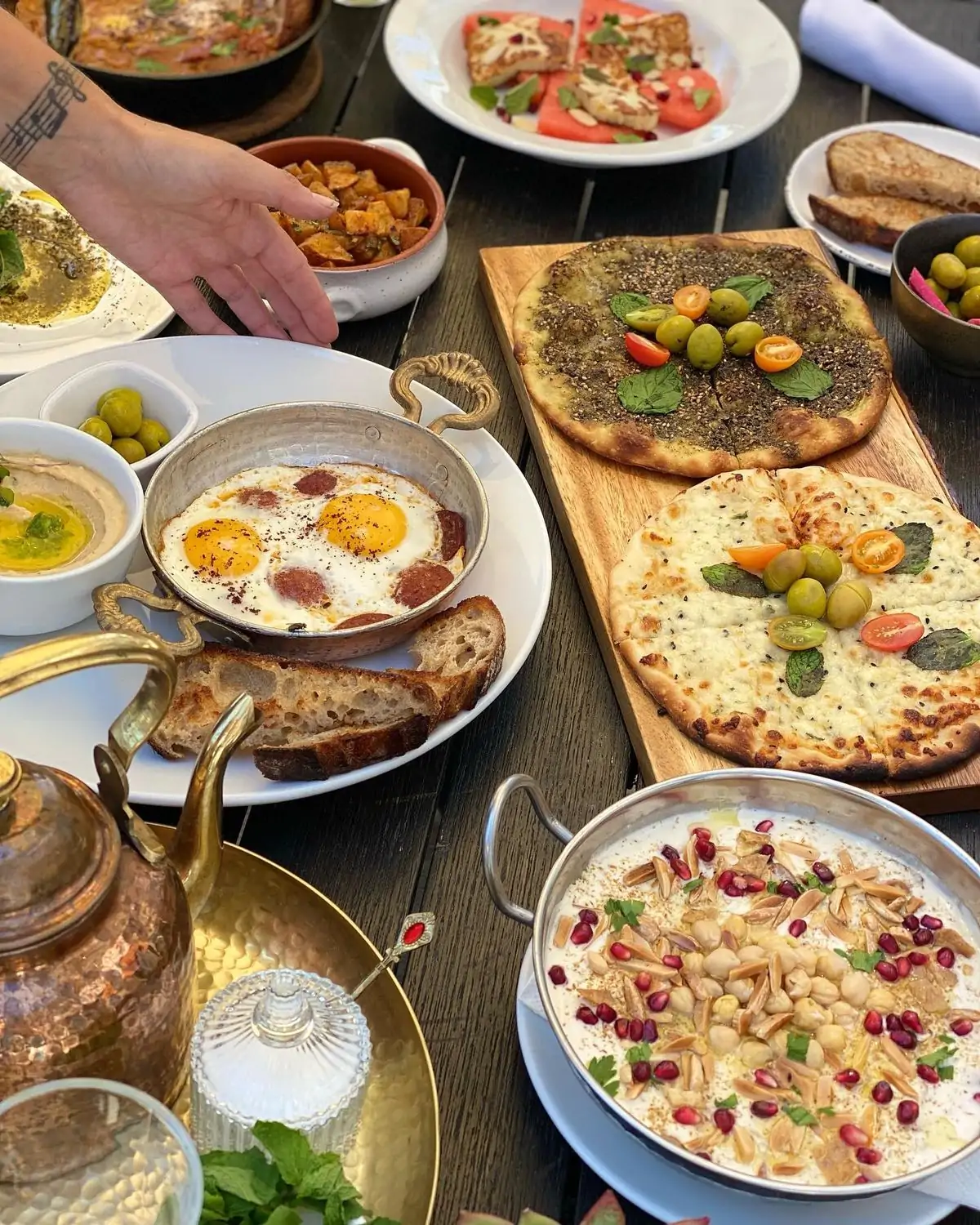 top-down view of a table spread with a variety of Middle Eastern dishes, including flatbreads, dips, salads, eggs, and a pot of tea at AMMATOLI in Los Angeles, now available to book on OpenTable.