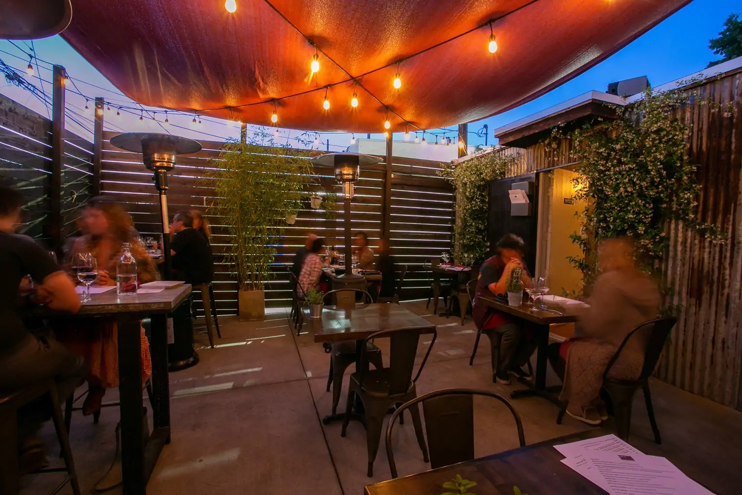An active with two-person tables and high tops with space heaters and plants lining the shelter at 401K Food and Wine in Los Angeles you can book on OpenTable.