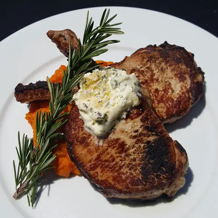 A bone-in steak cut sits on a white, round plate on a bed of mashed sweet potatoes at Chamberlain’s Steak & Fish, one of the best steak restaurants in Dallas on OpenTable.