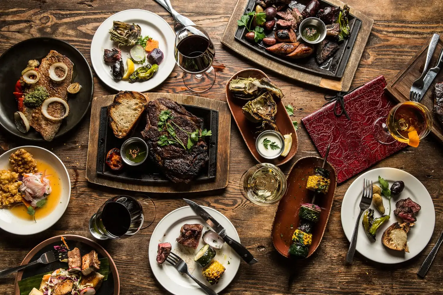 A table set with grilled steak, skewered corn, yams and sausage, and half-eaten plates at Lolinda, one of the best steak restaurants in San Francisco, on OpenTable.