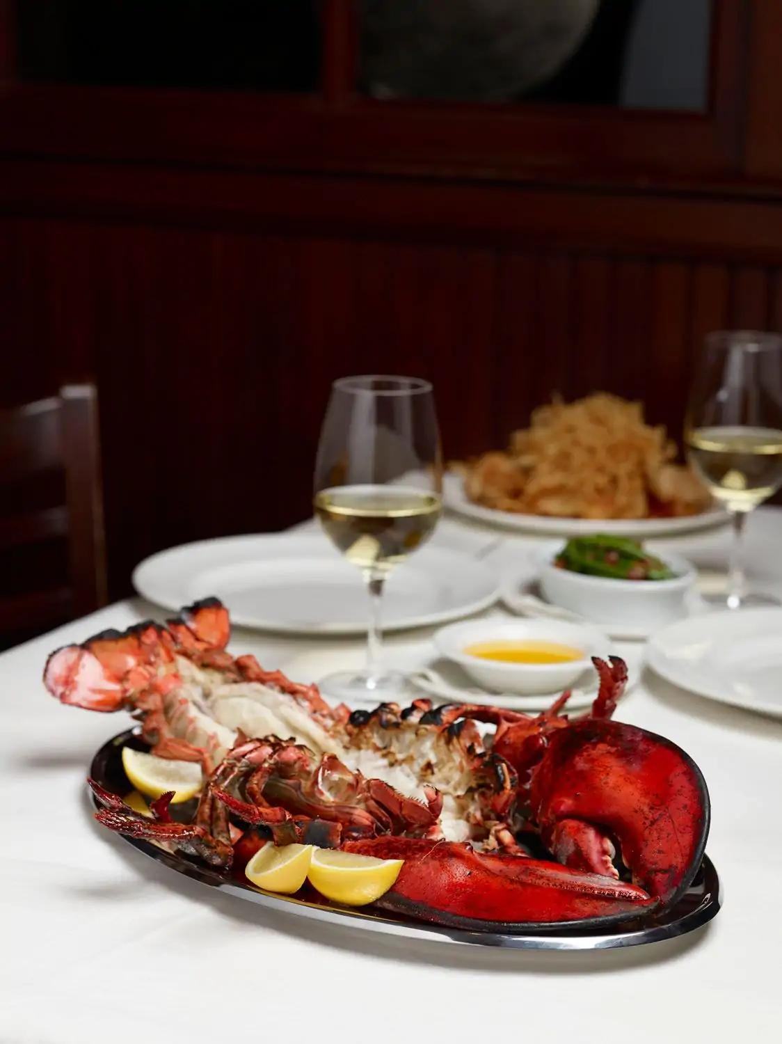 A broiled jumbo lobster lays on a silver platter with lemon wedges as a bowl of butter dipping sauce and glasses of white wine adorn the table at The Palm Washington DC in Dupont Circle, DC. Reserve on OpenTable.