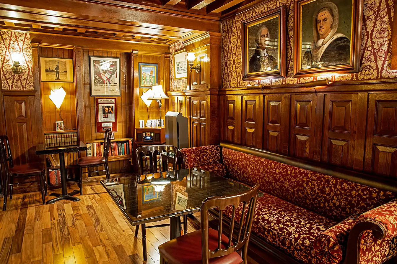 At Tabard Inn in Dupont Circle, DC, there is a cozy lounge area with red velvet sofas with gold accents, wood paneling, old books, and historic art on the walls—book on OpenTable.
