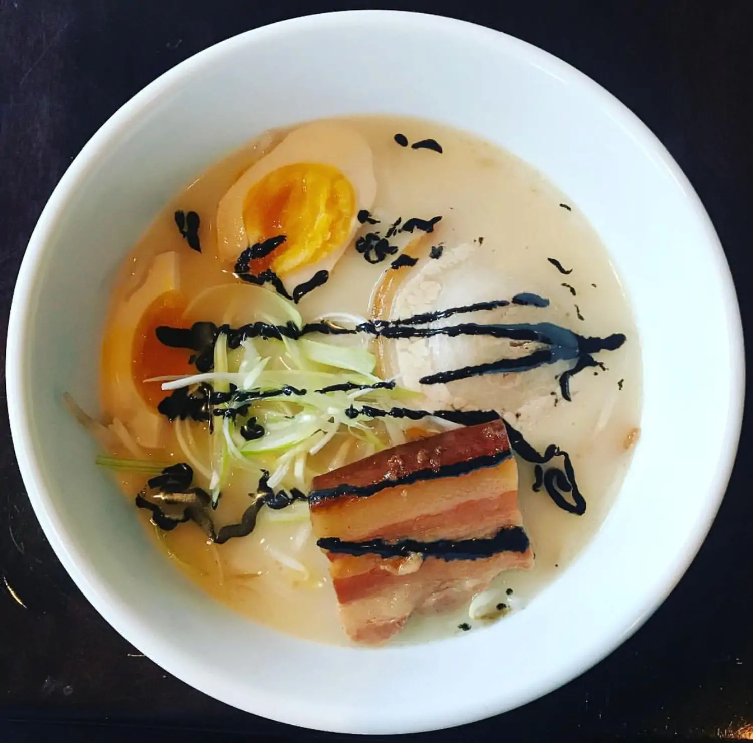 Top-down view of a bowl of creamy ramen with a marinated egg cut in half, sliced pork belly, and chopped scallions at Chaplin, one of the best Japanese restaurants in DC, available on OpenTable.