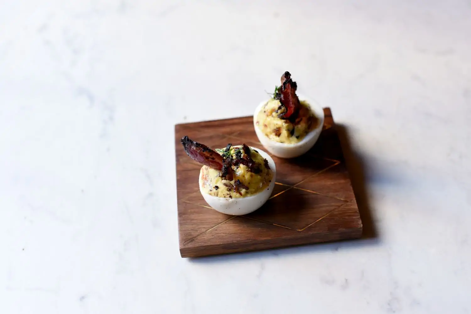 A small, wooden square holds two deviled eggs topped with pastrami at 2nd Floor Bar & Essen, among the best kosher restaurants in NYC on OpenTable.