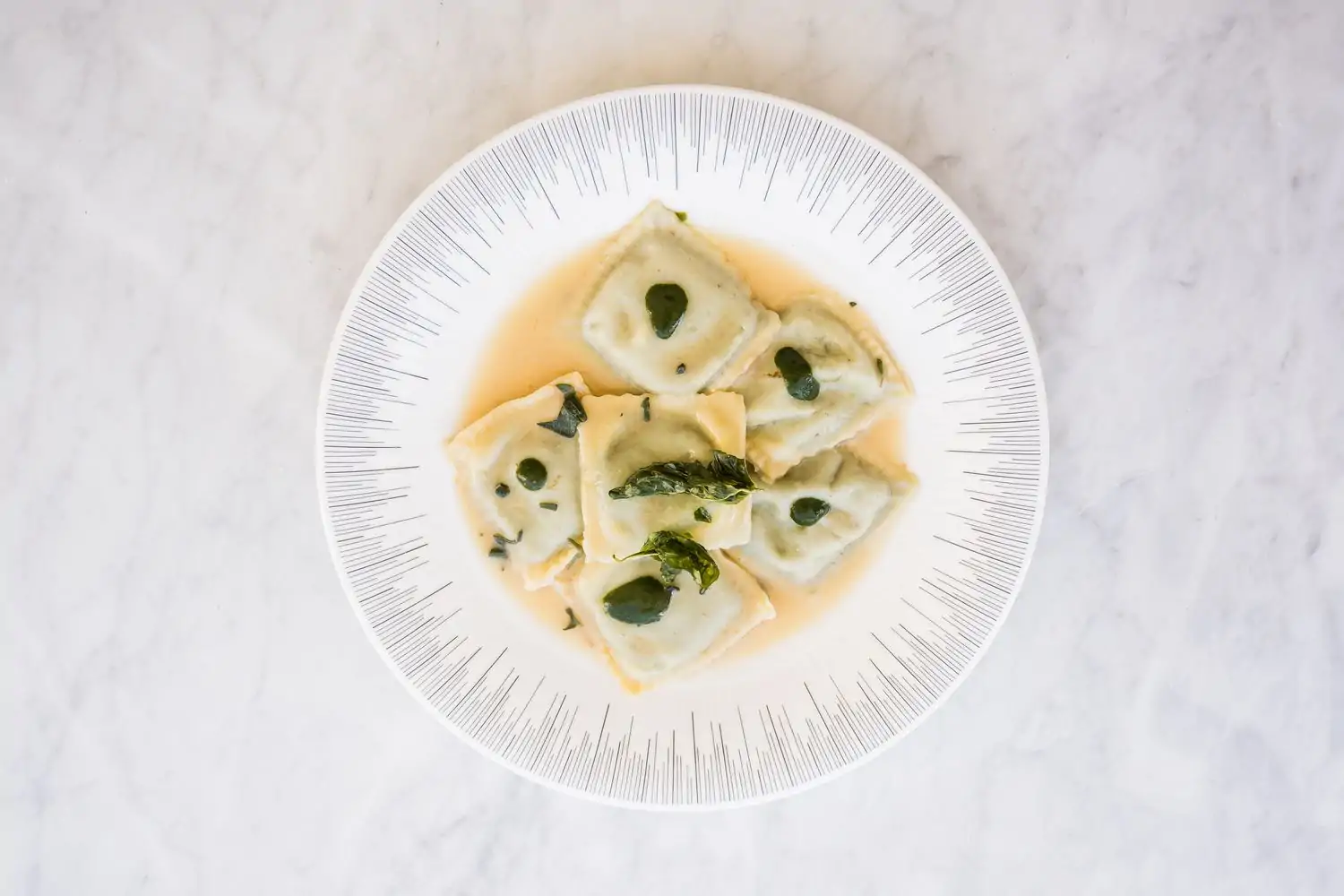 A birds-eye view of an elegant white plate with large pieces of ravioli topped with green garnishes at La Tomate, one of the best restaurants Dupont Circle, DC. Book on OpenTable.