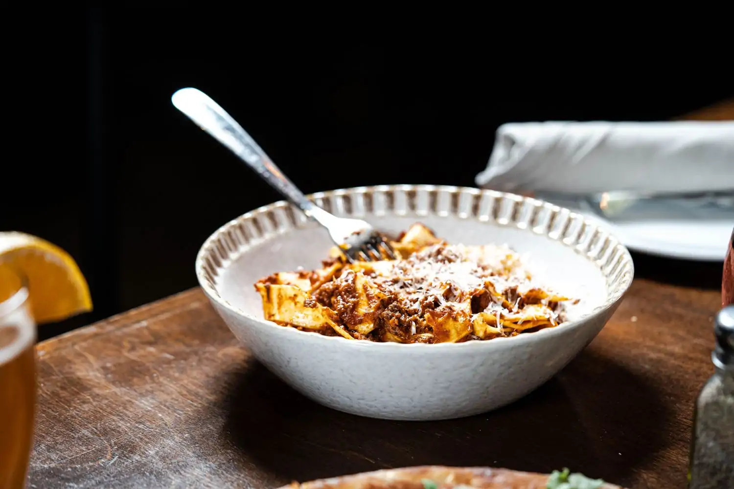 A rustic white bowl is filled with noodles and Bolognese sauce, drizzled with shredded cheese, while a fork is sticking out, at Sette Osteria, one of the best restaurants Dupont Circle, DC—book on OpenTable.