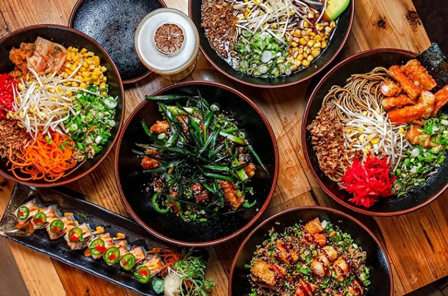 A wooden table is covered with elegantly presented Japanese dishes, including sushi, noodles, colorful vegetables, and seafood, at Sushi Tokyo, one of the best kosher dairy restaurants in NYC, found on OpenTable.