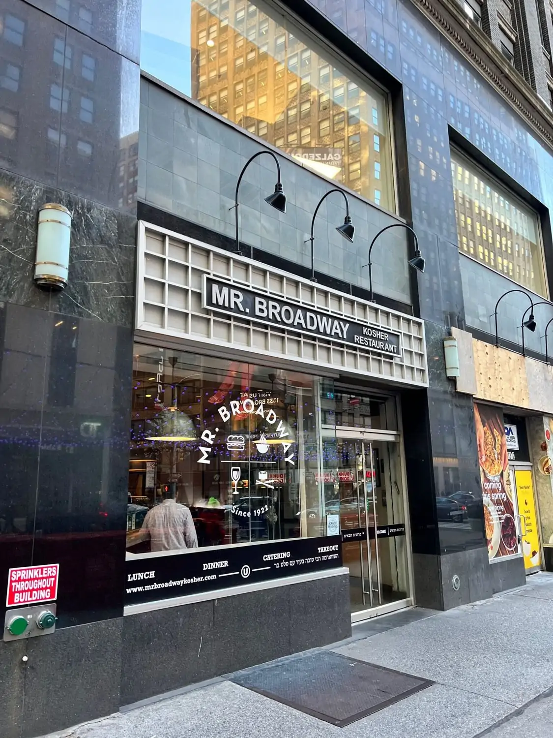 View of the large glass window and door at the city street entrance of the black marble building housing Mr. Broadway, one of the best kosher restaurants in NYC, on OpenTable.