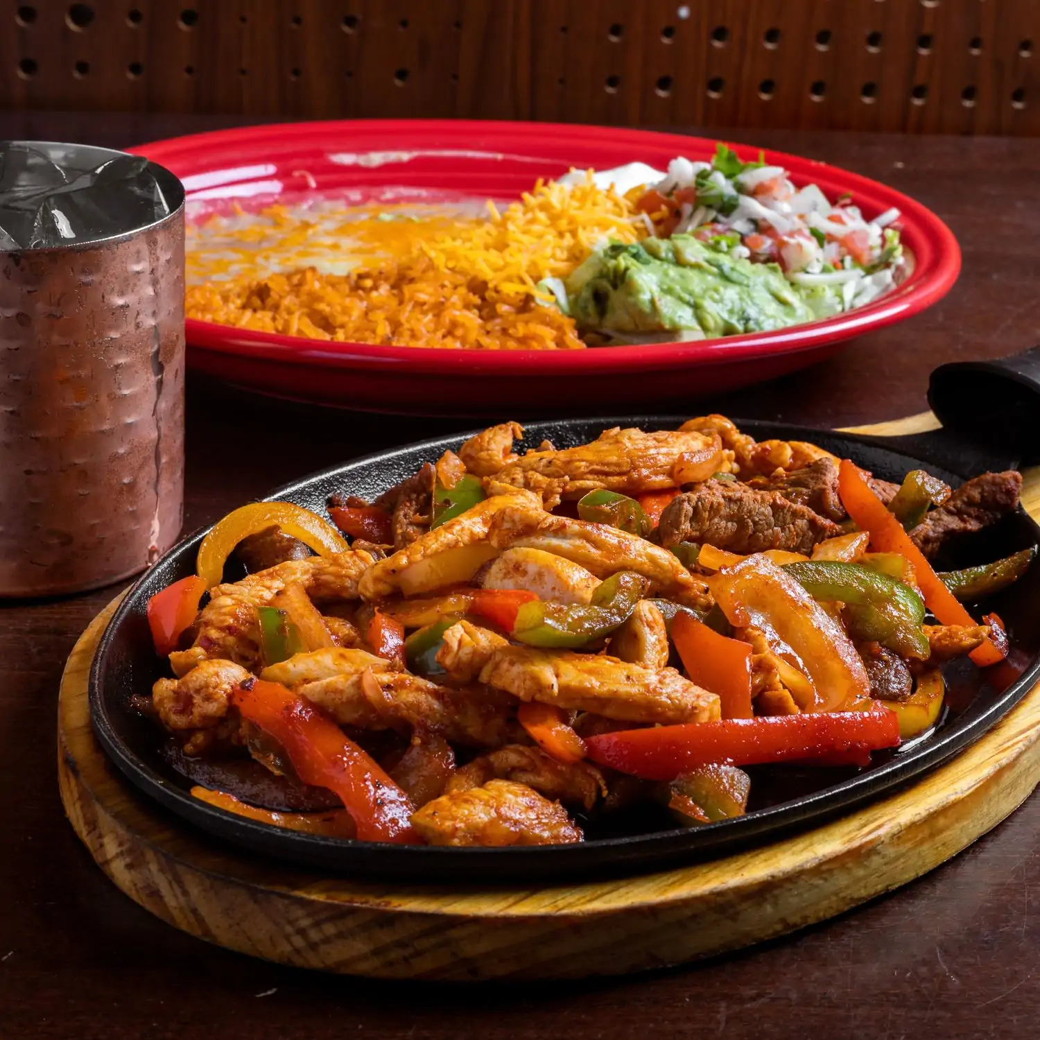 A picture of cooked meat strips with sliced peppers on a black iron cast pan with fixings of guacamole, salsa, rice, and shredded cheese on the side at 3 Margaritas - Downtown Denver(Downtown/LoDo), one of the best Mexican restaurants in Denver, CO. Reserve a table on OpenTable.
