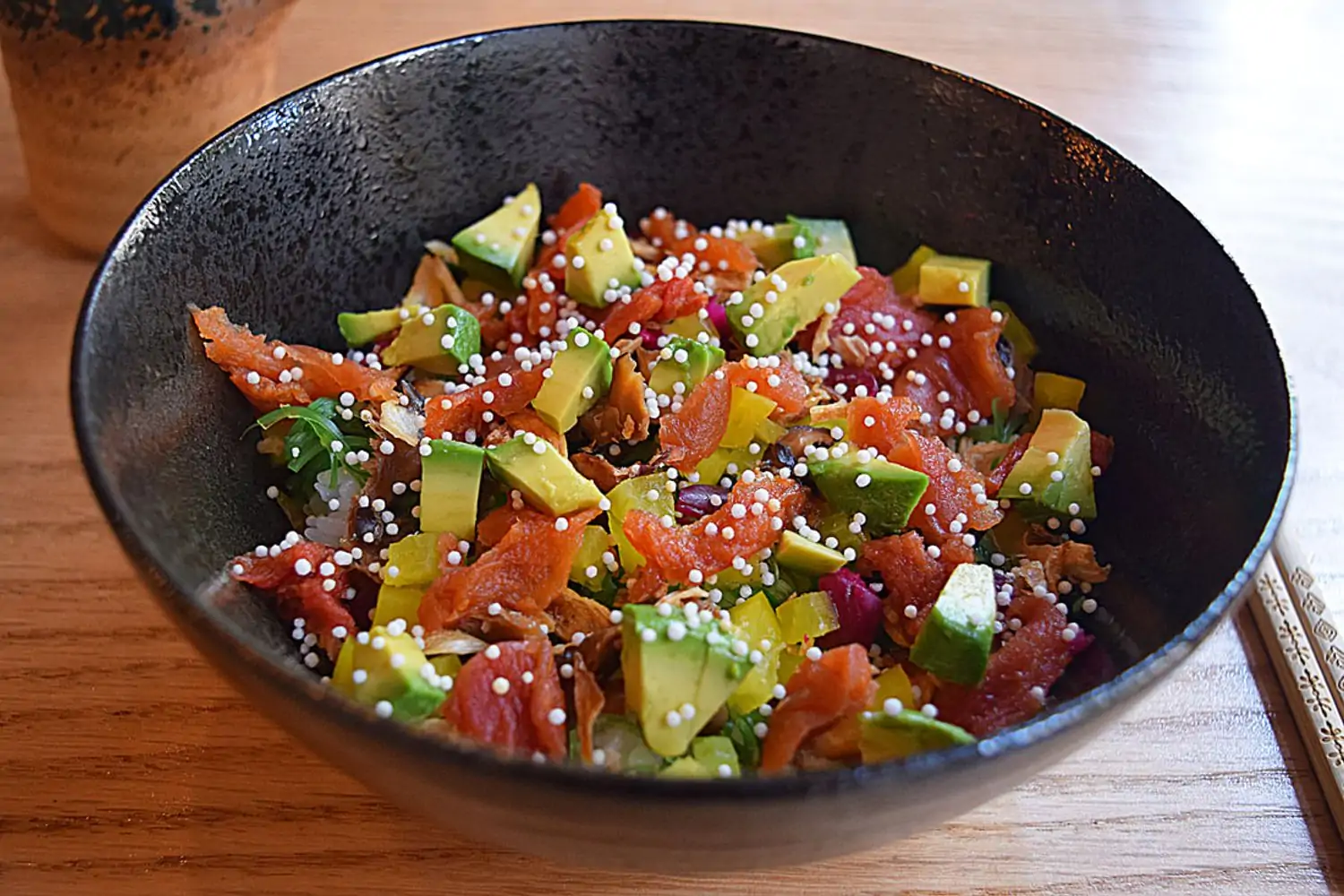 Close-up of a poke bowl with diced avocado, salmon, seaweed salad, and puffed rice, with chopsticks visible on the side at Tomo Sushi & Ramen, in Philadelphia. You can book on OpenTable.