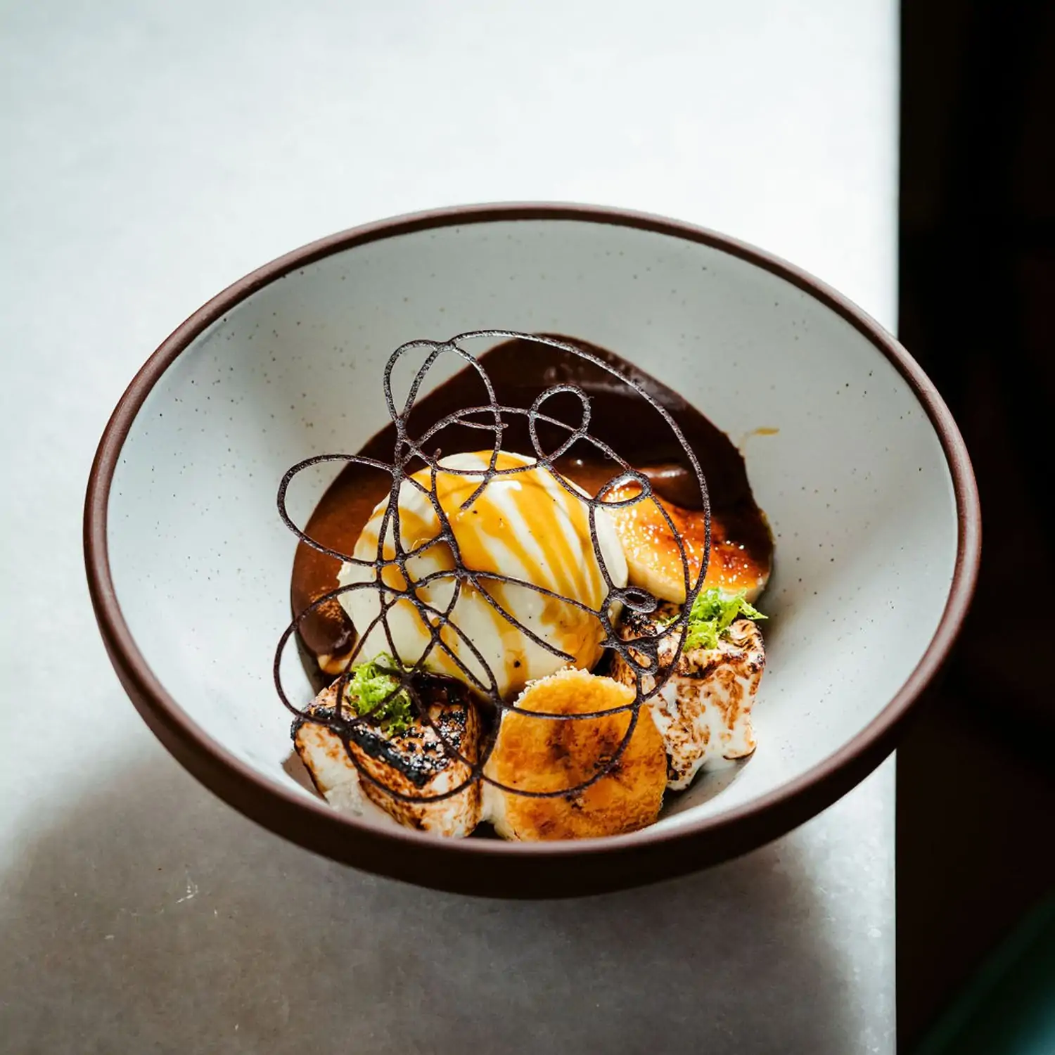 A bowl with vanilla ice cream and chocolate sauce at Rania DC, a best MICHELIN Star restaurant in Washington DC on OpenTable.