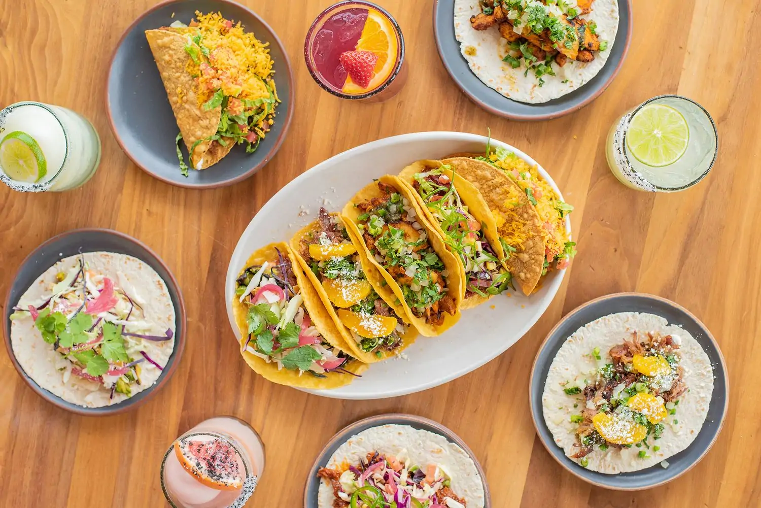 This aerial view showcases a table with Mexican platters, such as open-faced tacos stuffed with meat and fresh vegetables, and colorful drinks on the side, at Blanco Cocina + Cantina—Denver(Mayfair), one of the best Mexican restaurants in Denver. Book on OpenTable.