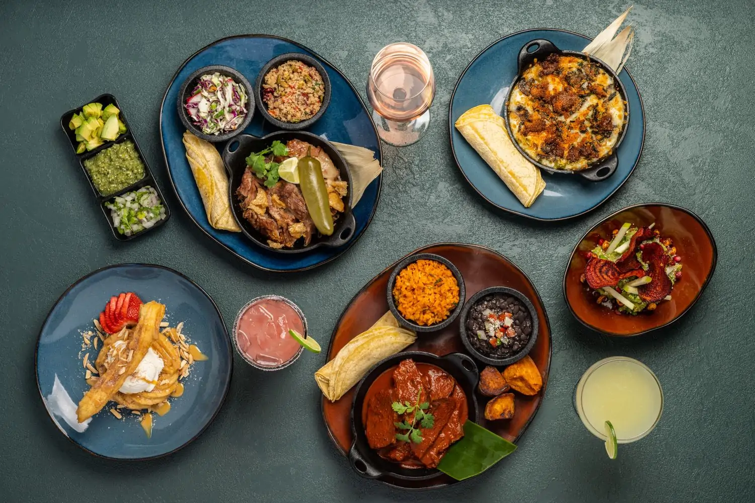 An aerial view of Mexican menu items like fajitas and carne asada platters with sides, tortillas, extra sauces, a beet side salad, cocktails, and a churro dessert from SOL Mexican Cocina – Denver (Cherry Creek). Book on OpenTable.