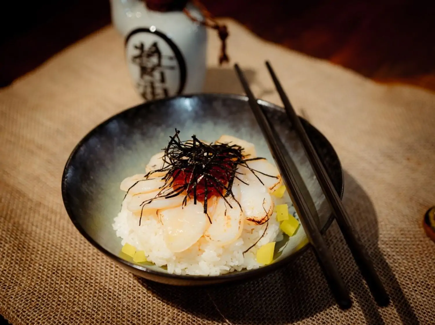 A black bowl with shrimp, seaweed, and pickled vegetables, served with a bottle of sake and chopsticks at Chicago's 312 Fishmarket, bookable on OpenTable.