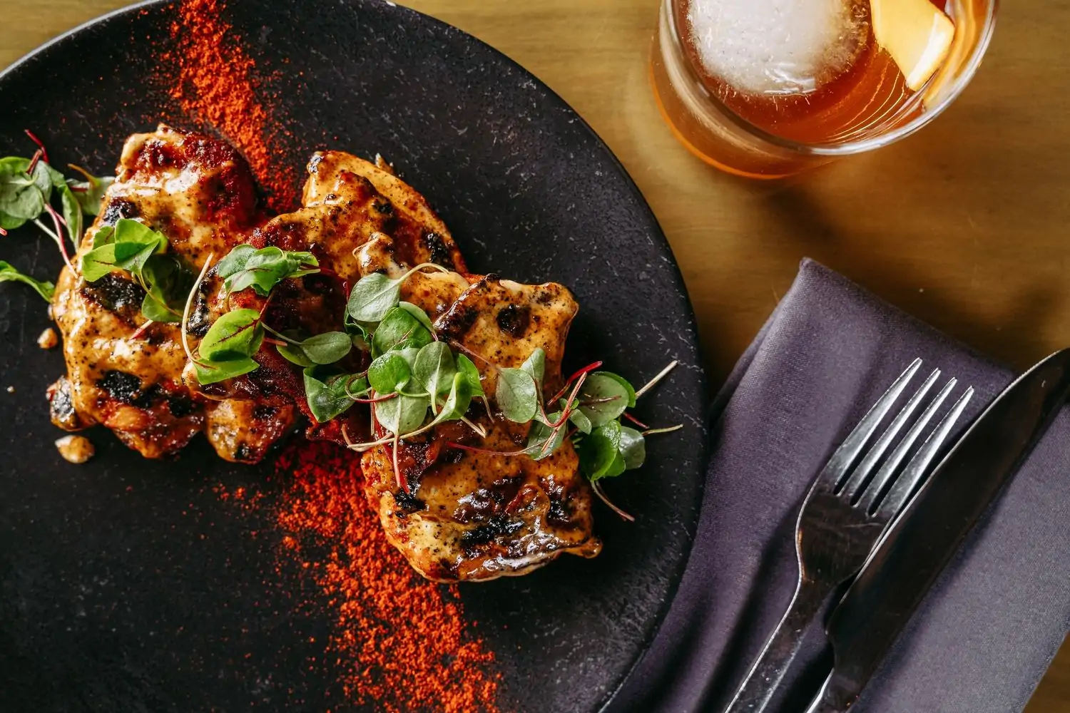 A plate containing pieces of grilled chicken with red spices and green garnish at Carson Kitchen, available on OpenTable.