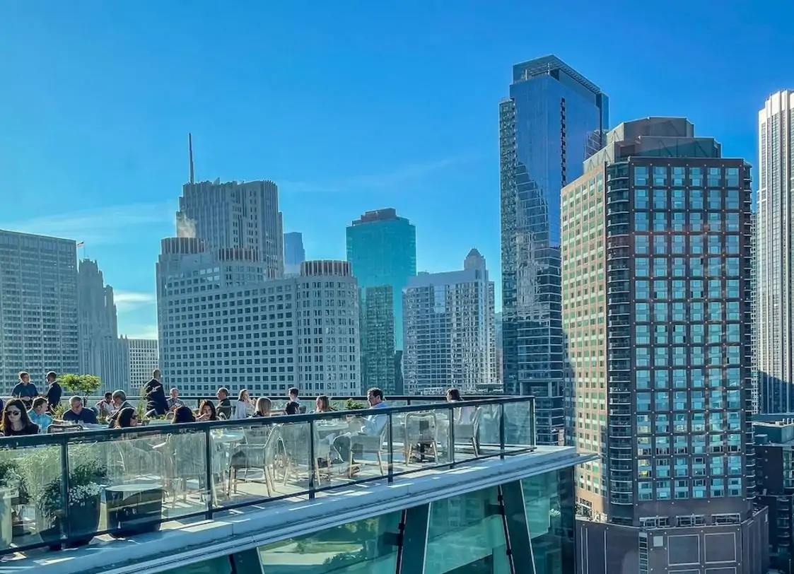 A rooftop restaurant with glass railings. There are patrons seated at tables enjoying a meal with a clear view of the cityscape, with tall buildings at Miru at the St. Regis Chicago—the best Japanese restaurant in Chicago, available to book on OpenTable and dine with a view.