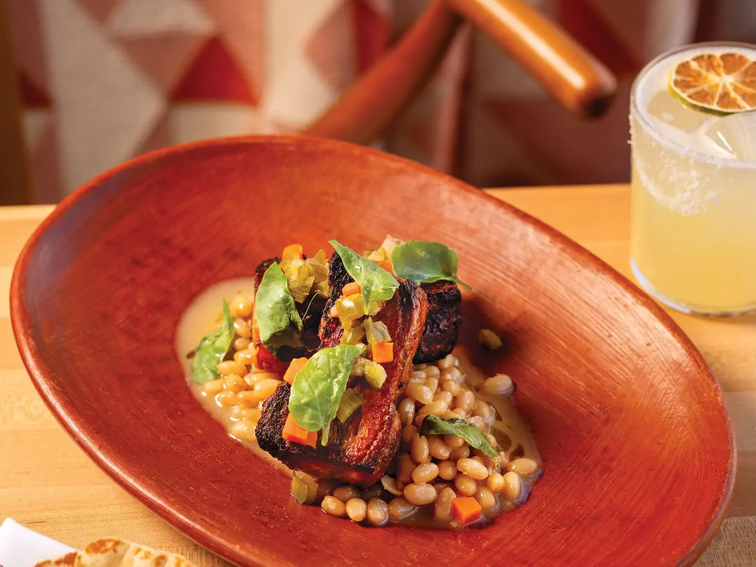 A close-up of a bowl of beans topped with a char-grilled item and garnished with chopped vegetables and herbs at Alma Fonda Fina, one of the best Mexican restaurants in Denver. Make a reservation on OpenTable.
