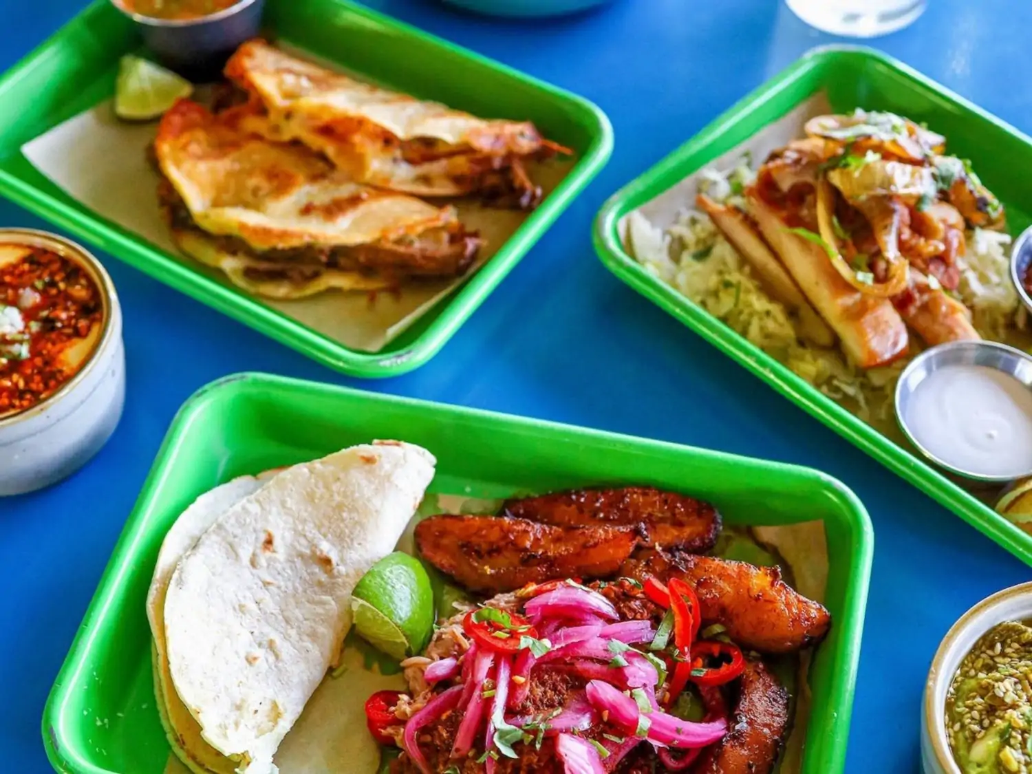 A close-up of several Mexican dishes made with tortillas and fresh vegetables on bright green platters at Mister Oso - RiNo, Denver, CO. Book on OpenTable.