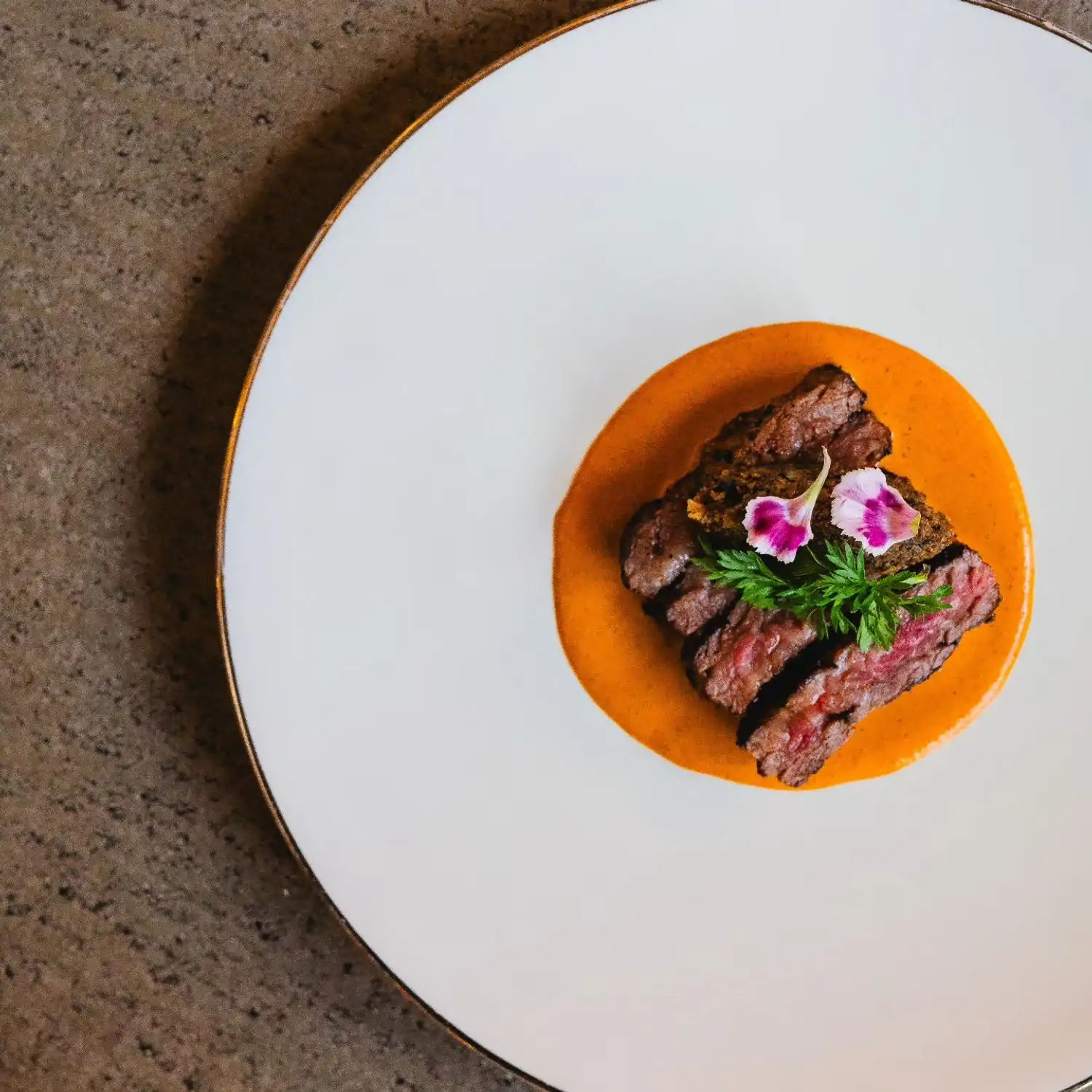 An aerial shot of slices of medium-rare beef sitting atop spicy salsa and garnished with parsley and edible flower petals at Xiquita, one of the best Mexican restaurants in Denver. Reserve a table on OpenTable.