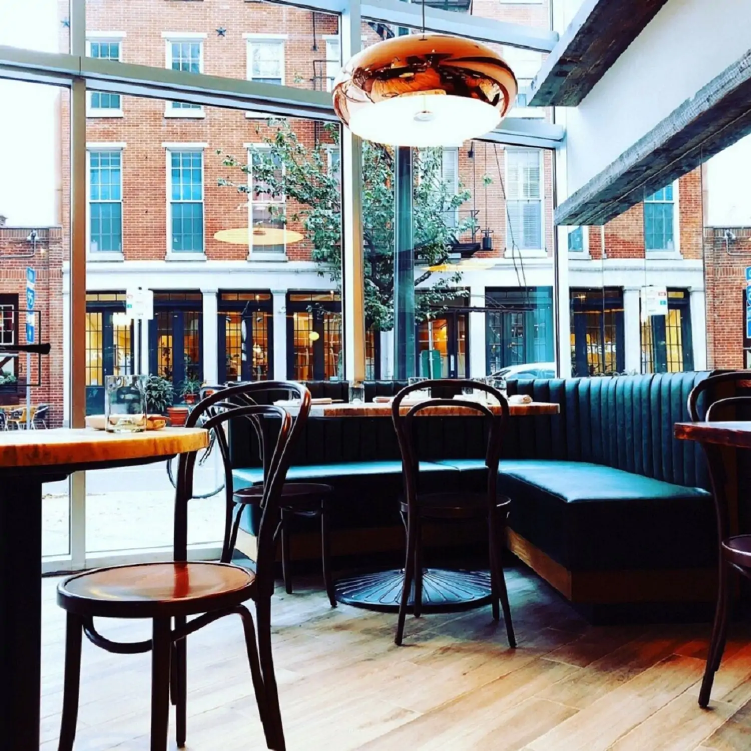 An airy dining room with wooden floors, booth seating, and a large window showcasing a cityscape with a brick building and trees at Tuna Bar in Philadelphia, one of the best restaurants in Philadelphia, to book on OpenTable.