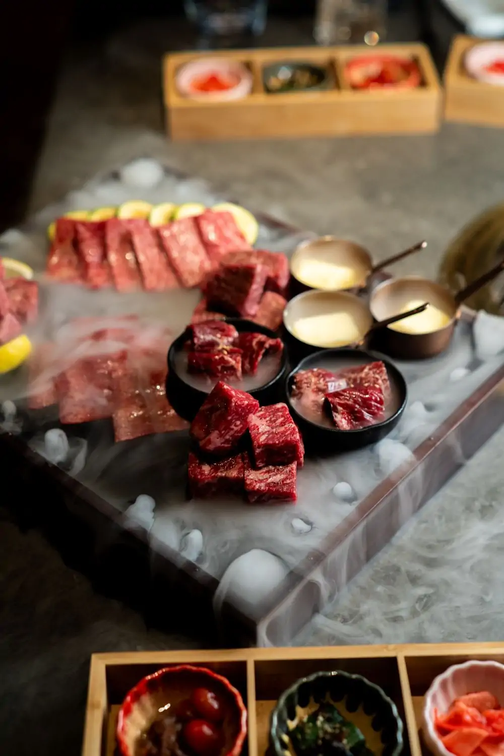 Grill up the finest cuts of Japanese wagyu right at your own table. Credit: Itadaki Yakiniku ALT text: Close-up of raw marinated beef short rib and other cuts of meat on a tray with dry ice smoke, accompanied by small bowls of dipping sauces at Itadaki Yakiniku, one of the best Japanese restaurants in Seattle, available to book on OpenTable.