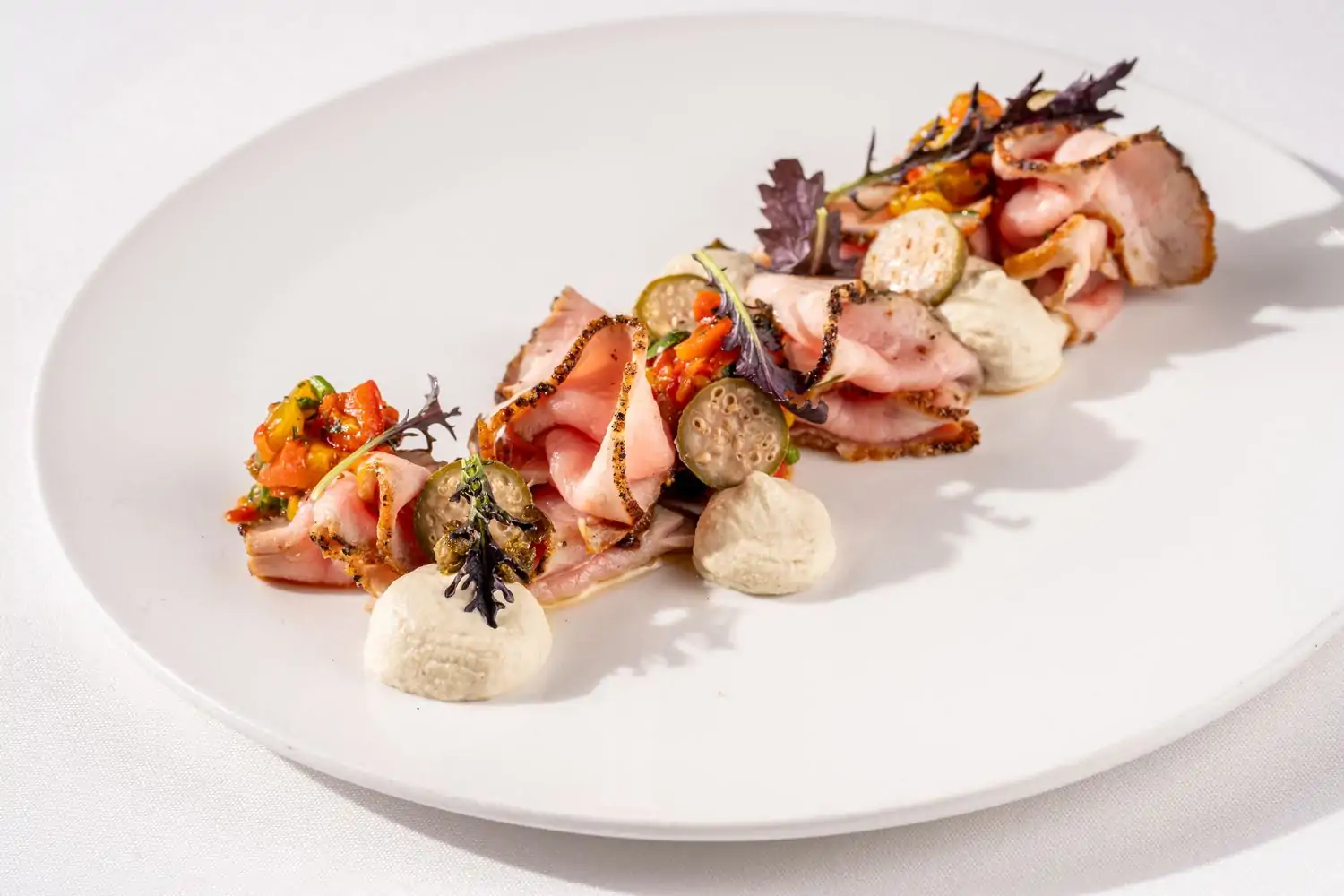 An artfully displayed dish from Barolo Grill, one of the best restaurants in Cherry Creek Denver. The dish is composed of thinly sliced meat, alternated with tomato relish and green garnish, displayed on a white plate—book on OpenTable.