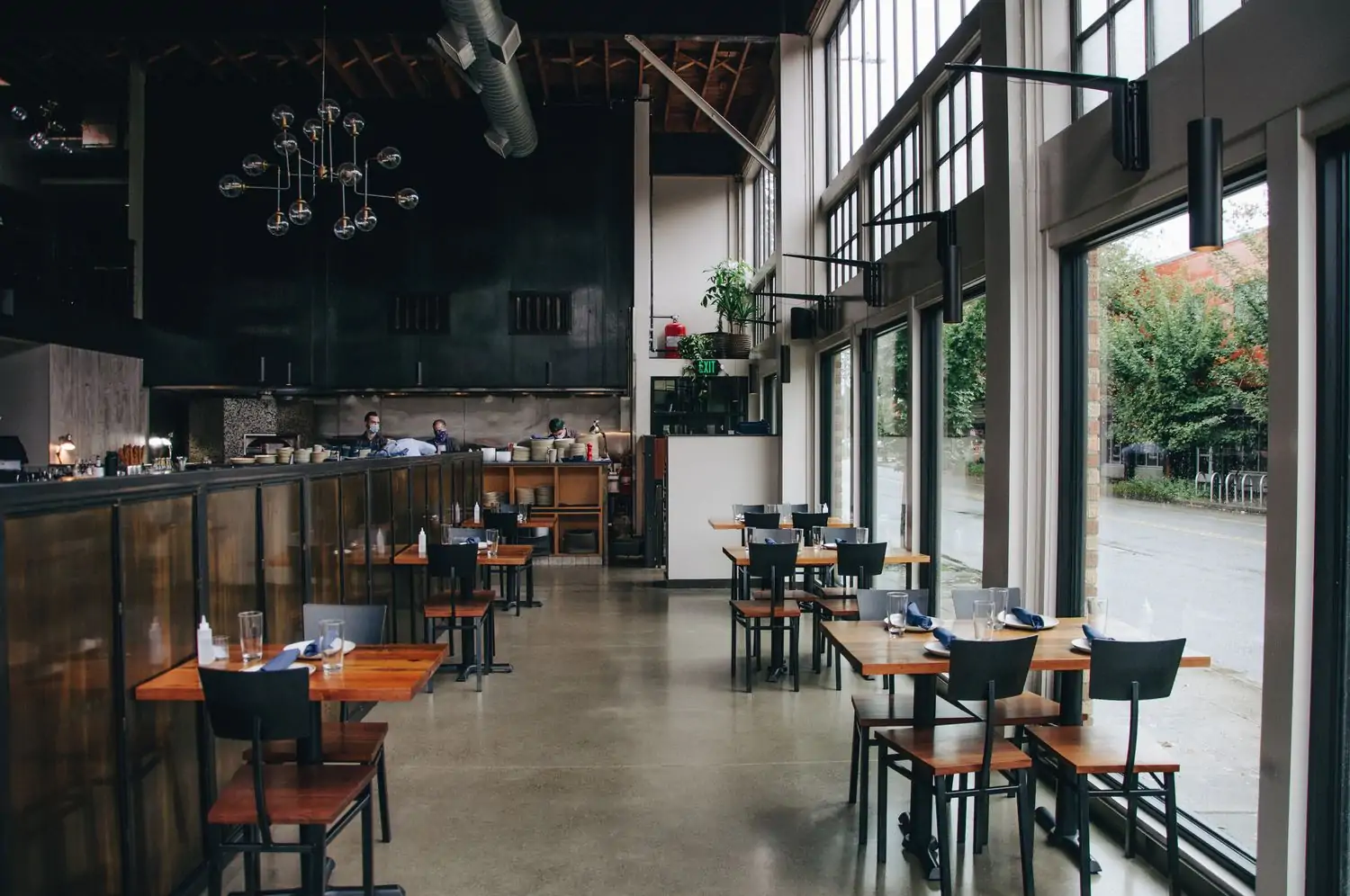 An industrial-style dining room with dark furnishings, black accents, and large windows on one side at FlintCreek Cattle Co., in Seattle. Book on OpenTable.