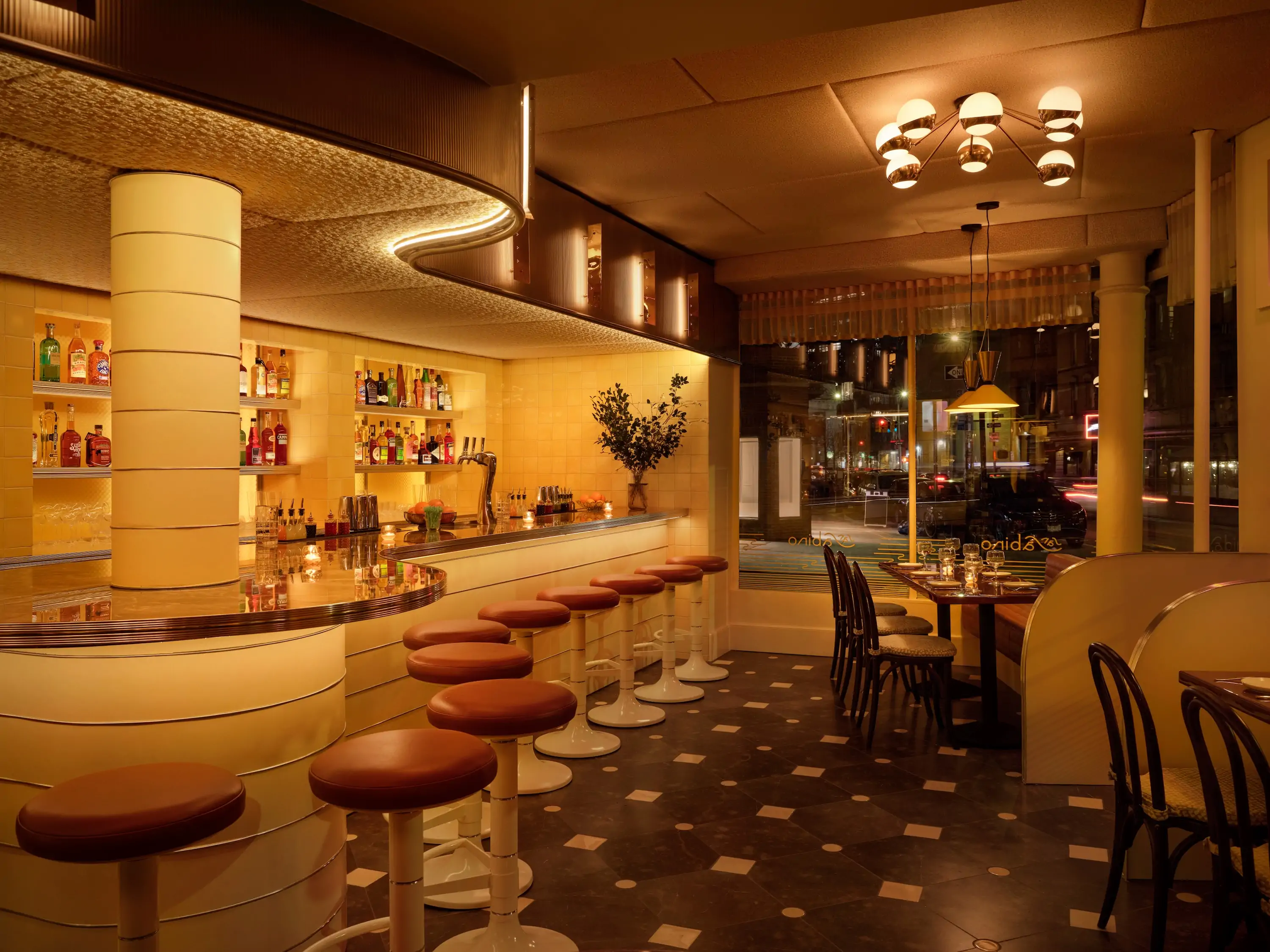 The interior of NYC restaurant San Sabino seen here with a curving bar and a large window that looks out on the street.