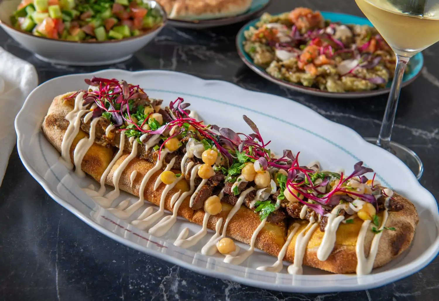 A plate containing fresh Mediterranean bread topped with meat, chickpeas, garnish, and sauce at Cafe Landwer, Los Angeles, found on OpenTable.