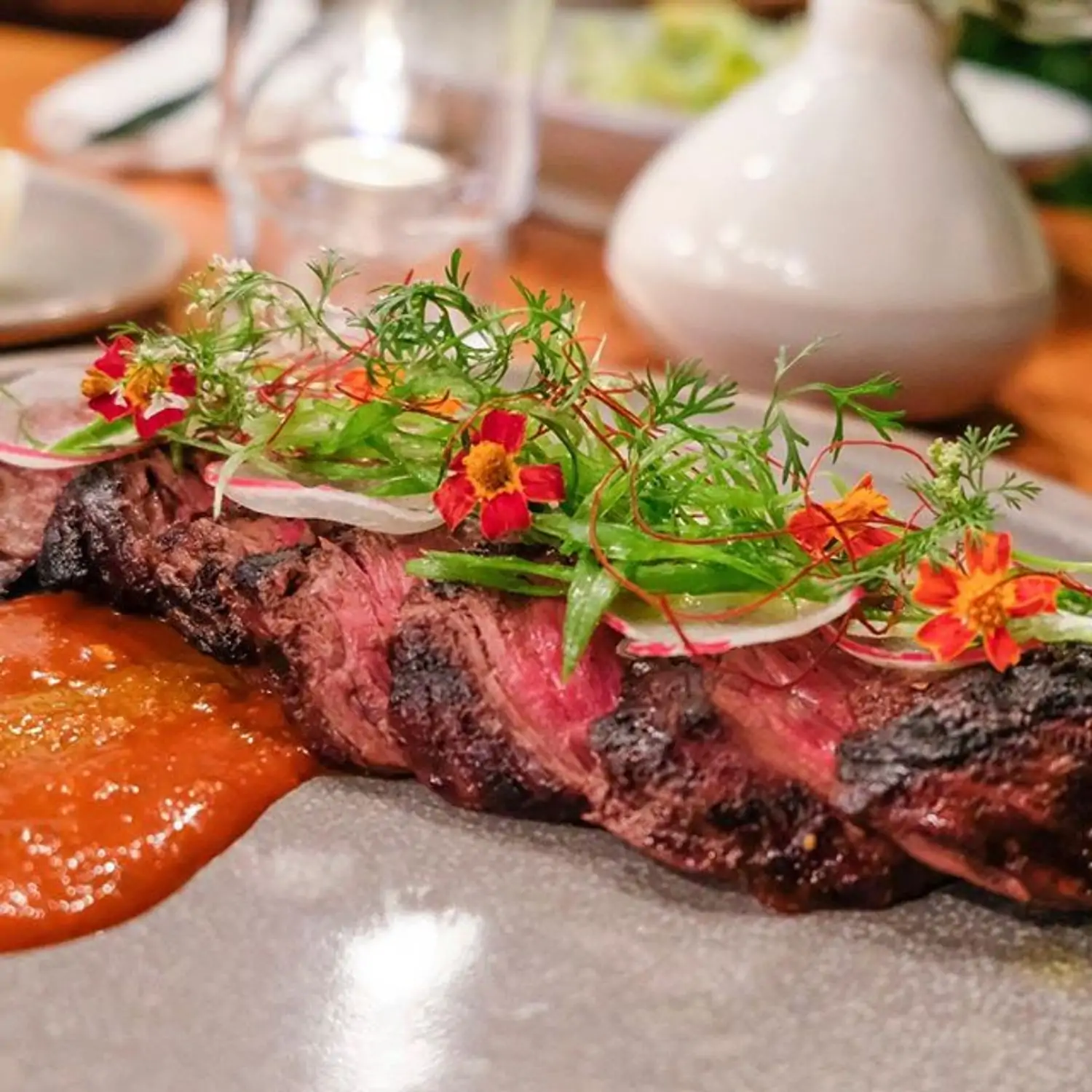 A plate containing slices of steak on top of a bed of orange sauce at Hinoki & The Bird, a great Century City restaurant found on OpenTable.