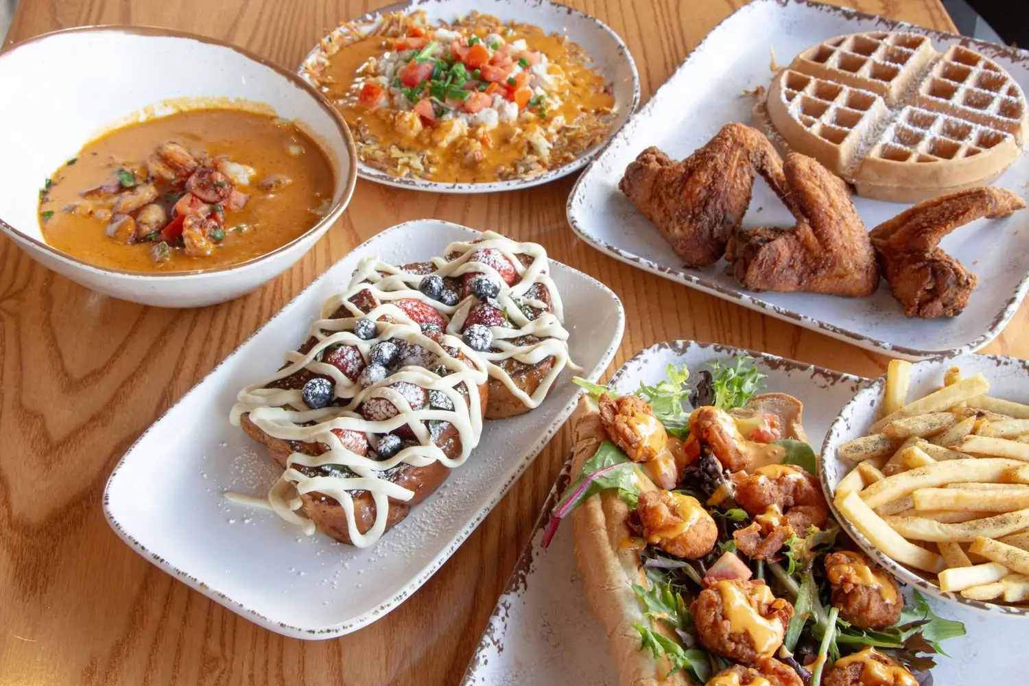 A table containing plates of French toast, fried chicken, sandwiches, and soups at Milk & Honey - The Wharf, Washington DC, available on OpenTable.