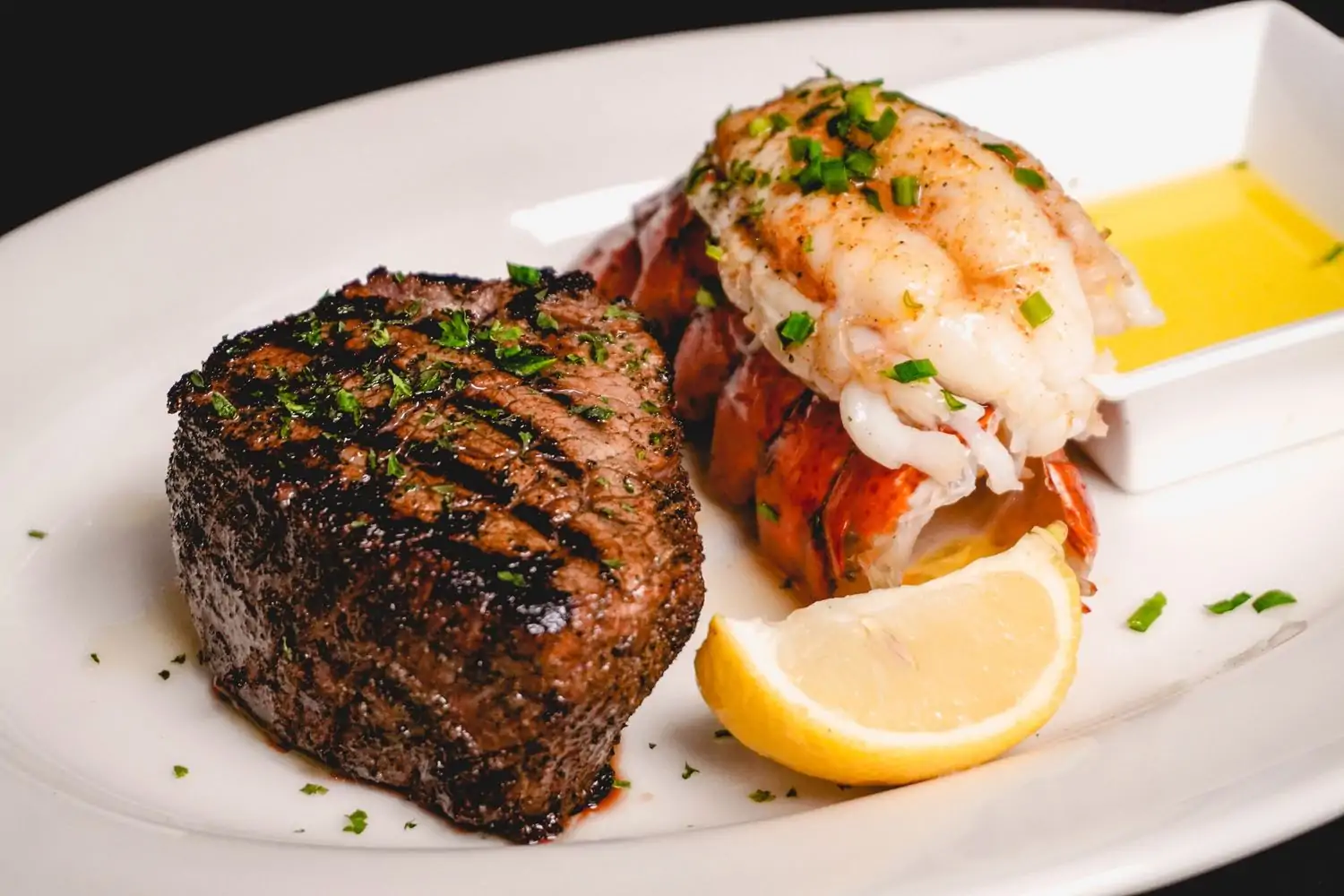 Surf and turf on a white plate with lemon and butter, entrees available at Little Joe's Steakhouse, in Honolulu. Book on OpenTable.