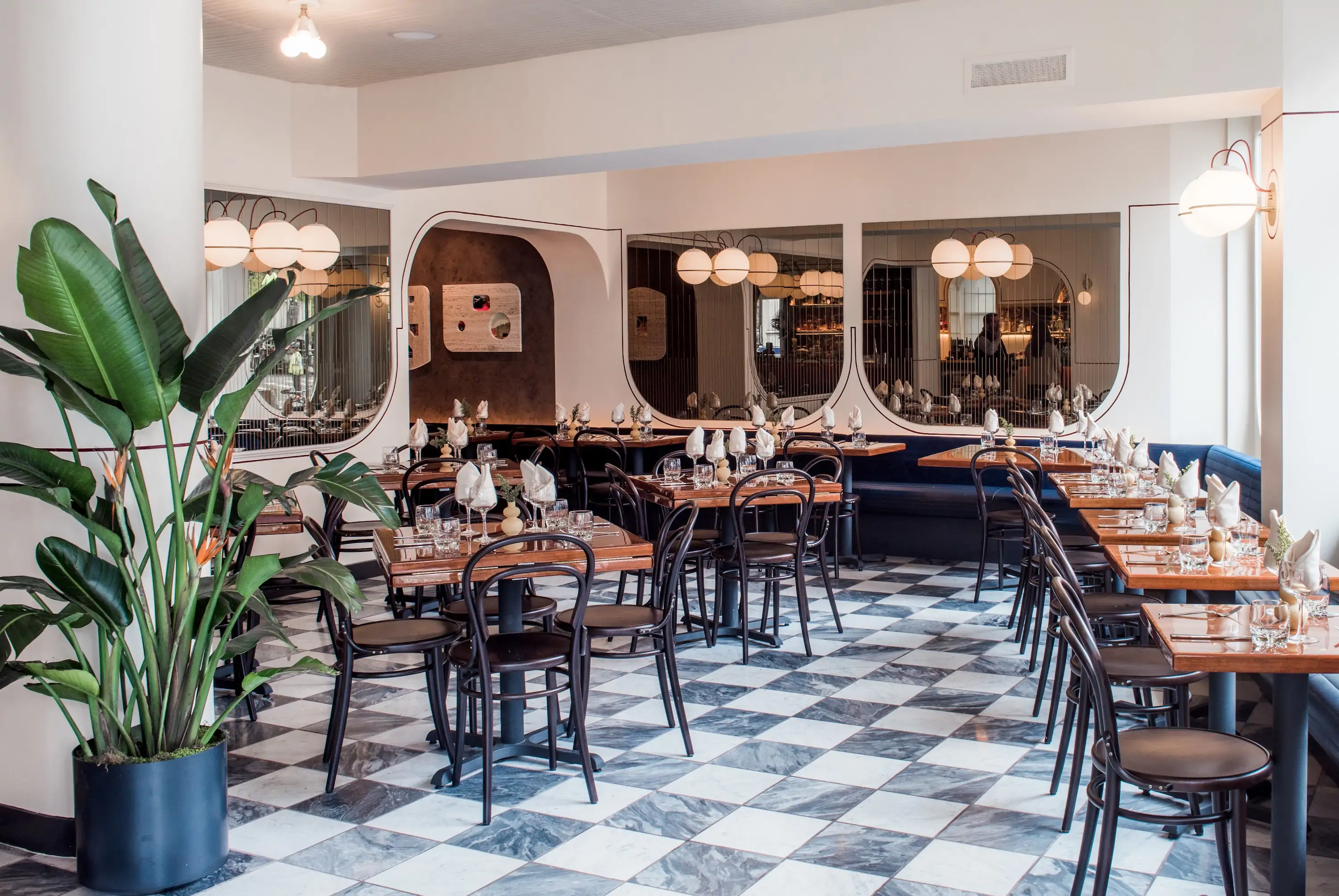 The interior of NYC restaurant Don Angie seen here with wooden tables and chairs, globe lights, and a marble checkerboard floor
