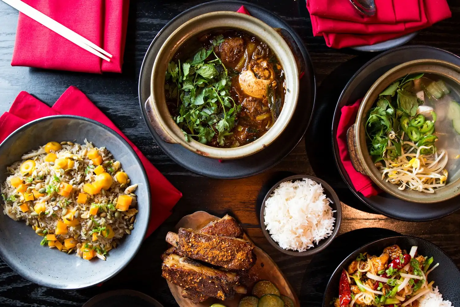 An aerial view of Chinese plates like ribs, rice dishes, stew, and vegetable soup alongside red cloth napkins at Old Thousand, in Austin. Available on OpenTable.