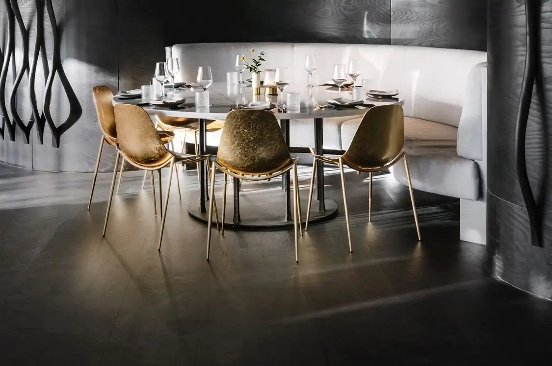 An oval, marble table, flanked by golden chairs and a white half-moon banquette at Arlo Grey by Kristen Kish, in Austin. Book on OpenTable.
