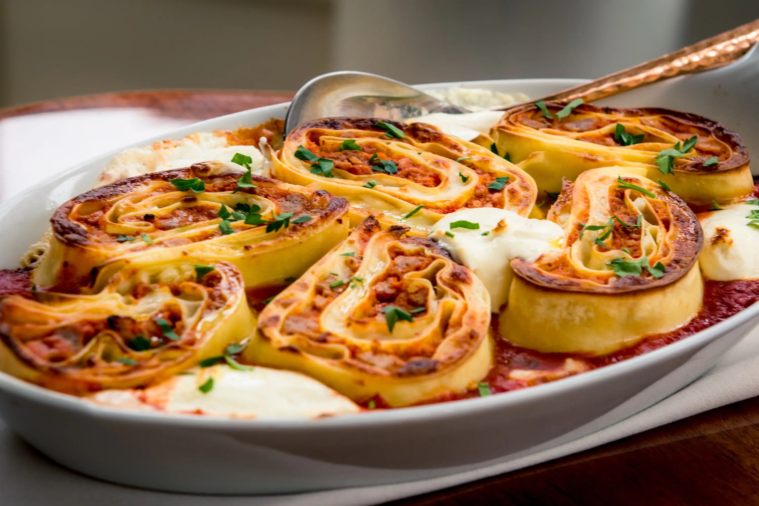 Spiraled, sliced pieces of lasagna with red sauce sitting in an oval plate at New York restaurant Don Angie