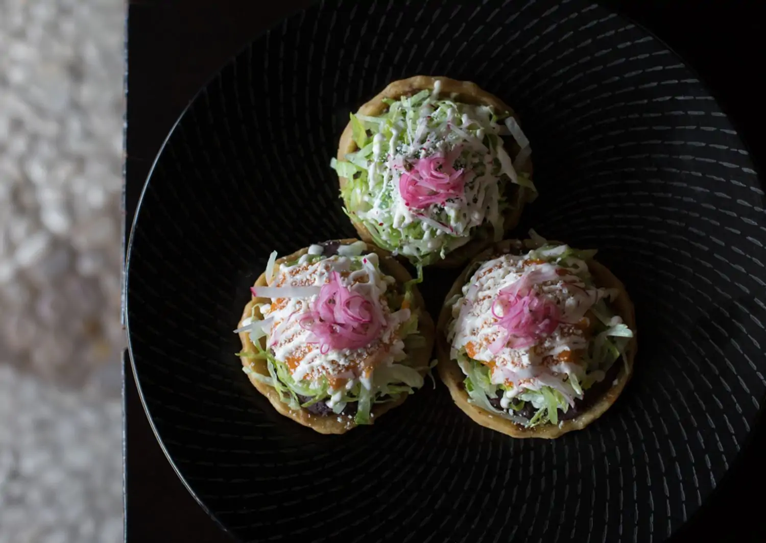 A plate containing three tortillas topped with beans, lettuce, cheese, and pickled onion at Javier’s, one of the best Century City Mexican restaurants, on OpenTable.