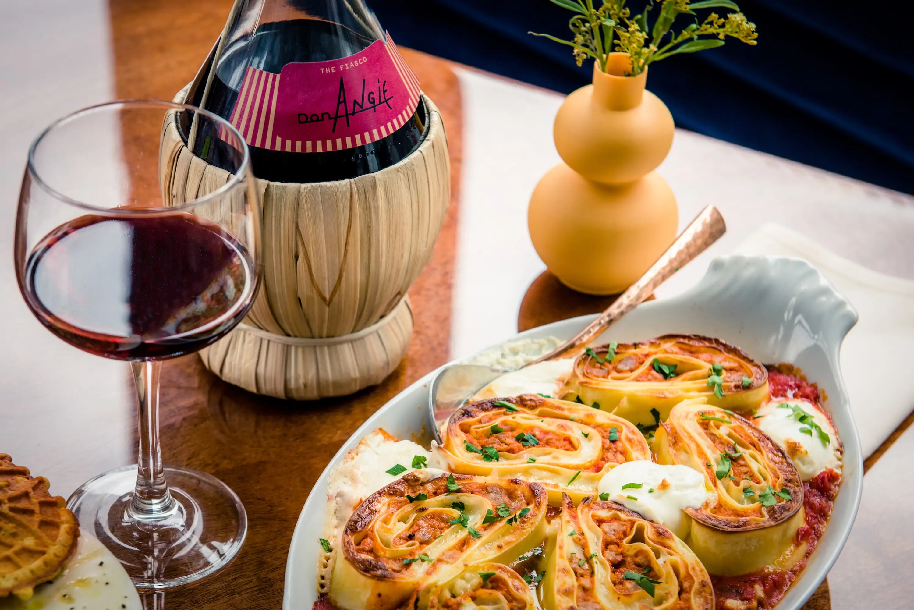 NYC restaurant Don Angie’s pinwheel lasagna on a table next to a bottle of wine