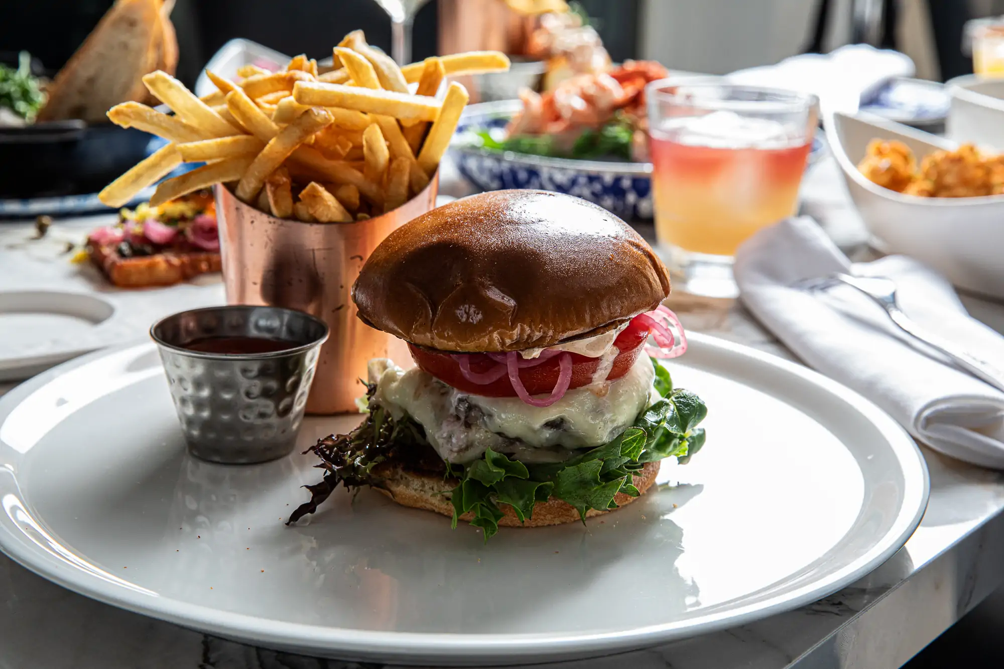 A tall burger placed on a white oval plate at Charleston restaurant NICO Oysters + Seafood