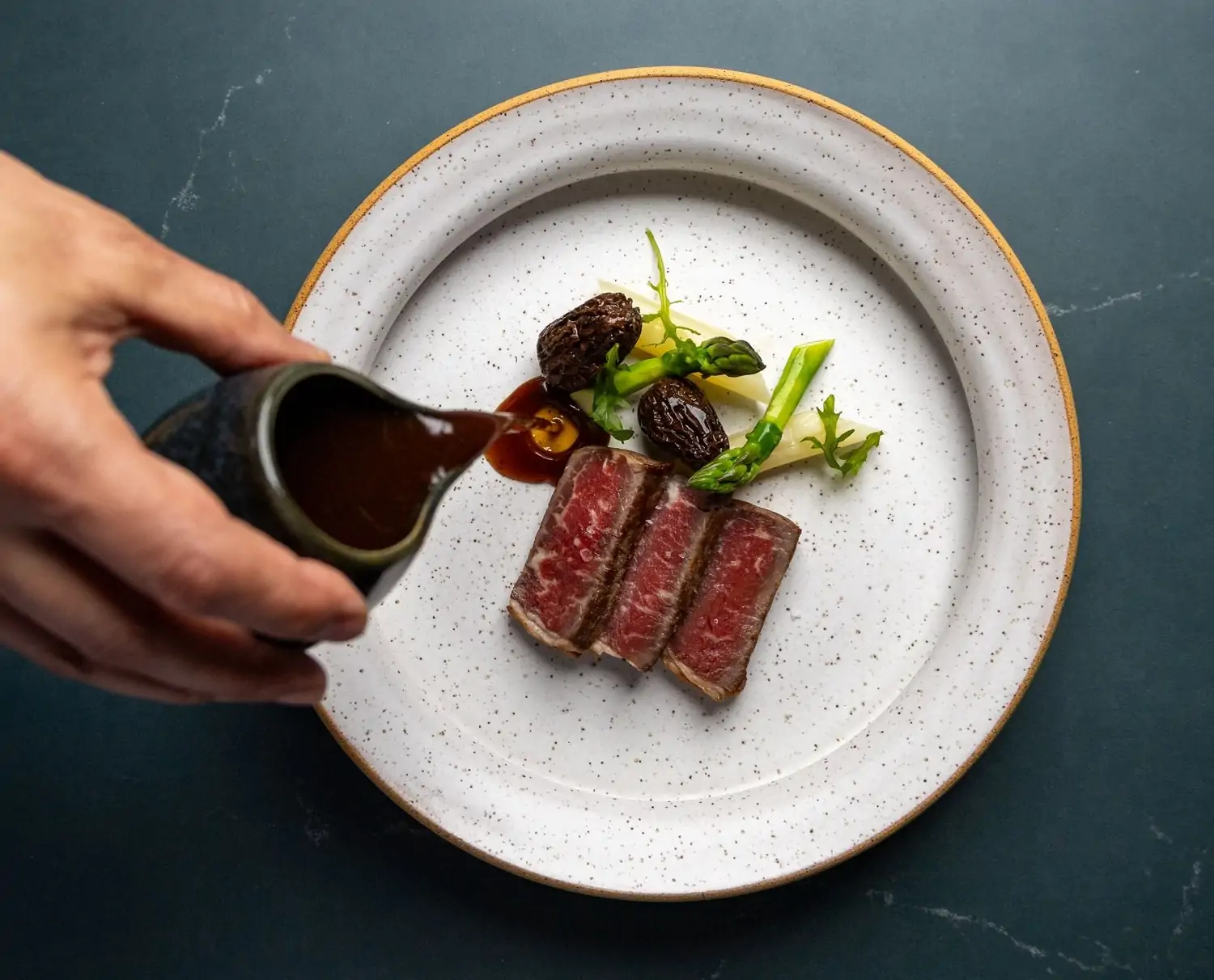 A plate of thinly sliced beef with brown sauce being poured on top