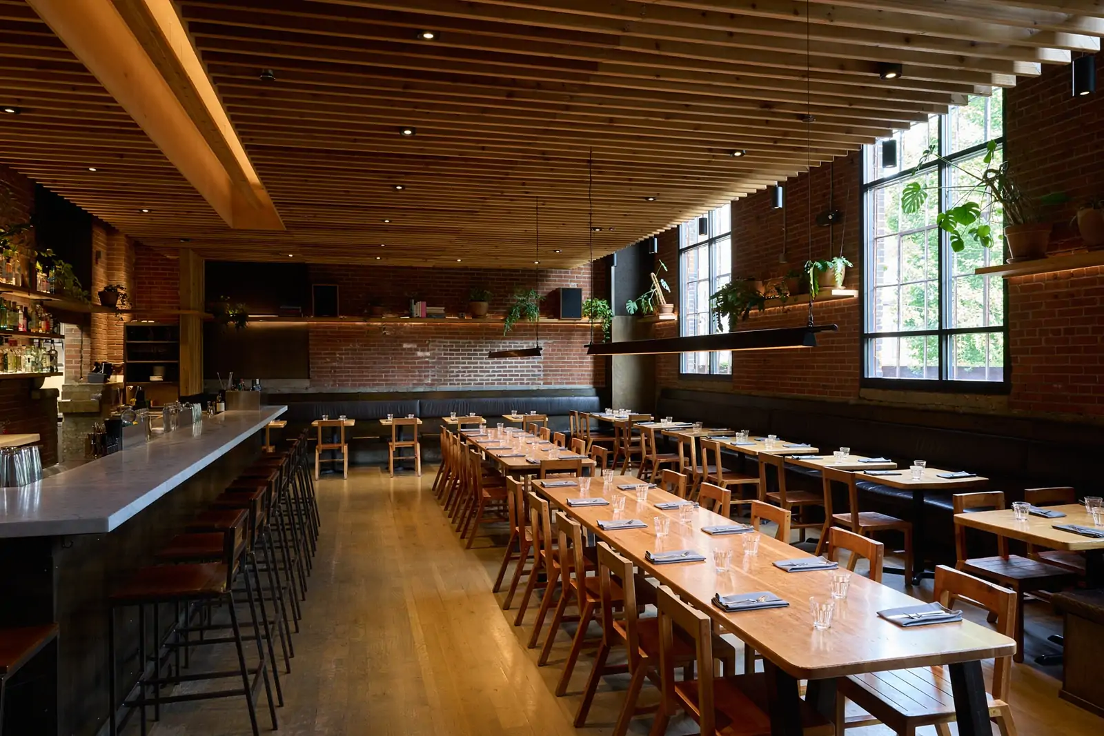 The interior of Nashville restaurant Rolf and Daughters seen here with a wooden ceiling, a marble bar, wooden tables and chairs, and a brick wall