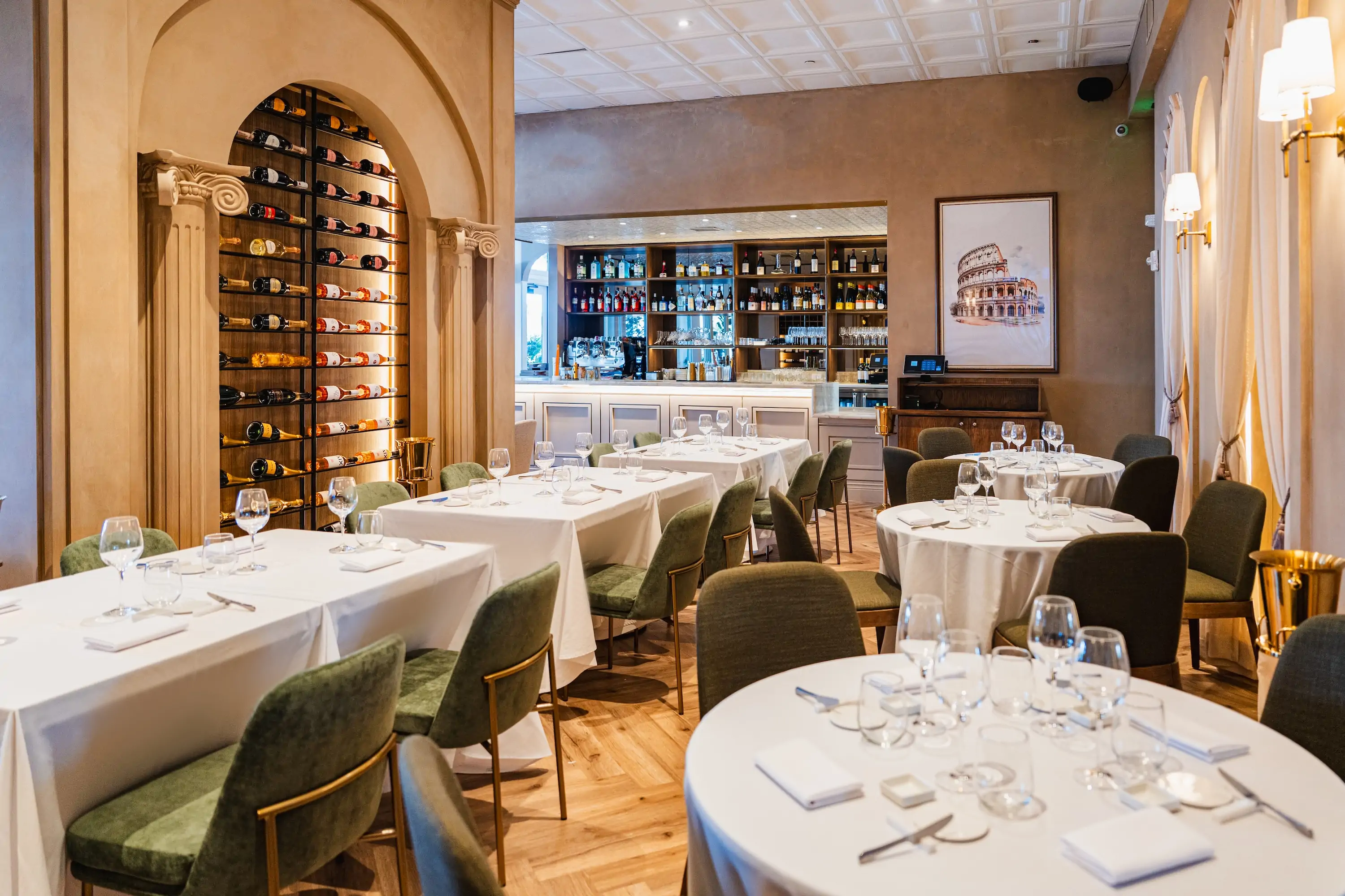 White tablecloth-covered round tables, a wine wall in the background, and arched windows make up the interior of Miami restaurant Novatore