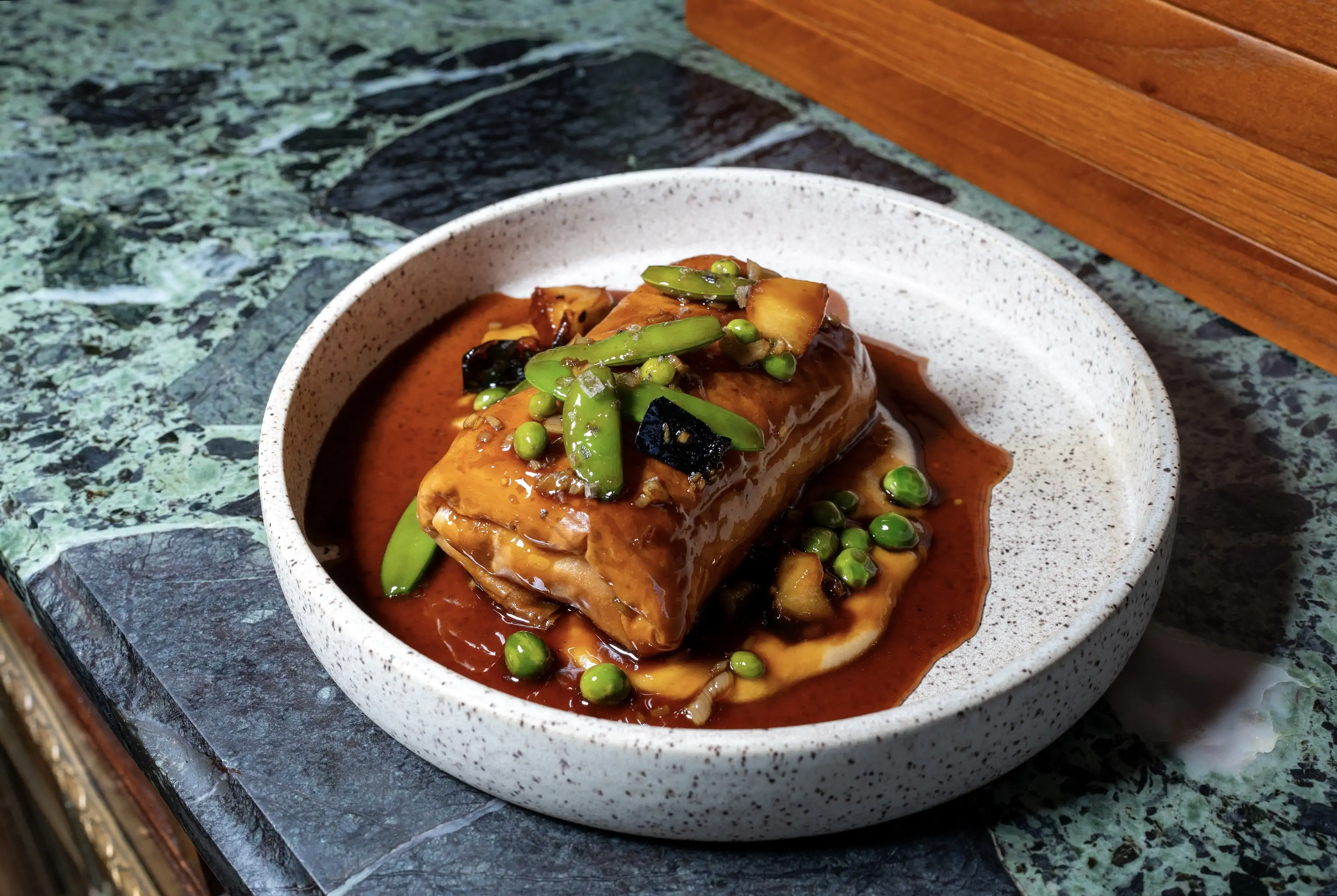 A filled lamb pie sitting in a pool of sauce with greens and beans at Philadelphia restaurant Emmett
