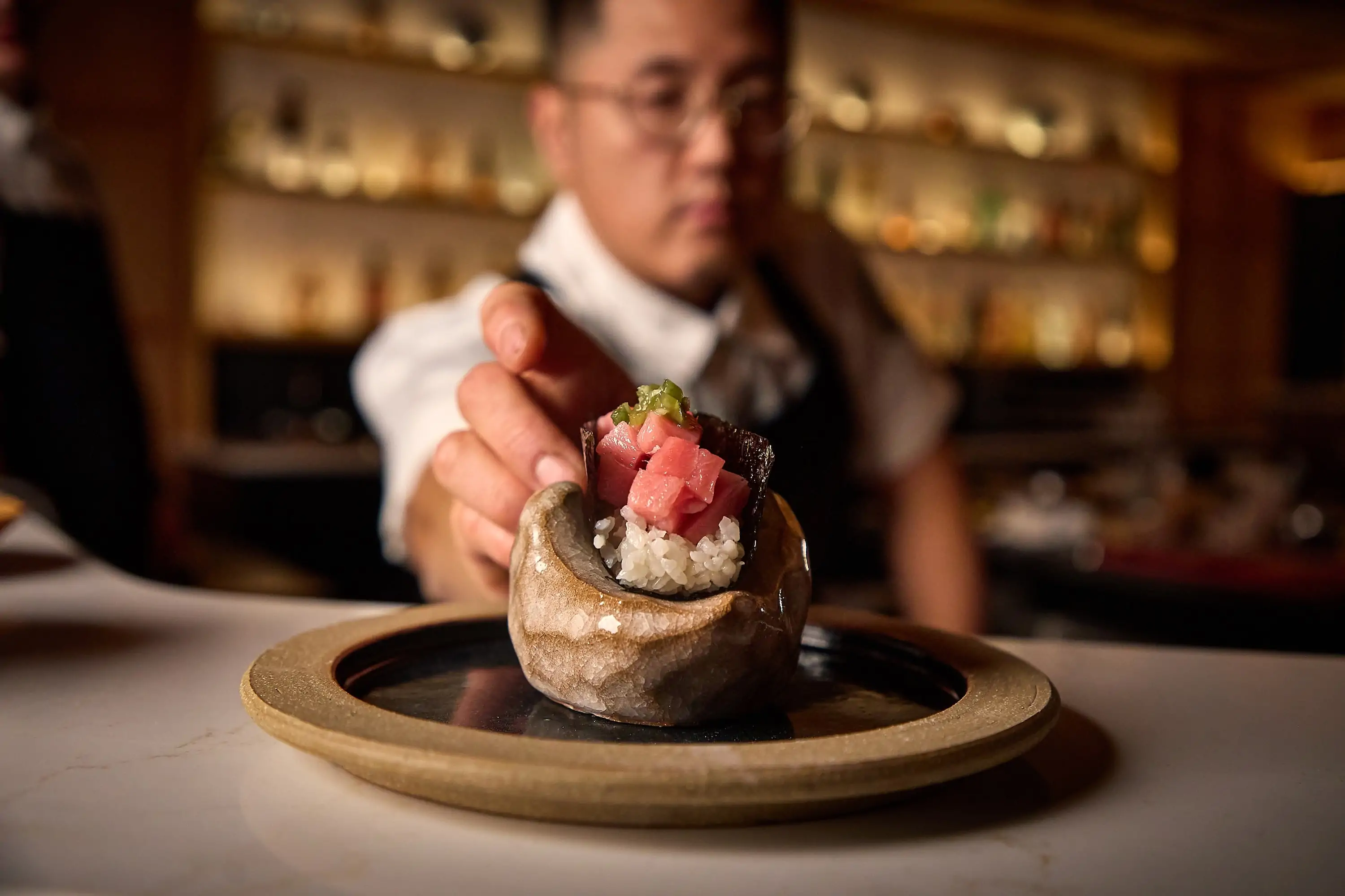 A sushi handroll being placed on a marble counter by a chef at Chicago restaurant NORIKO