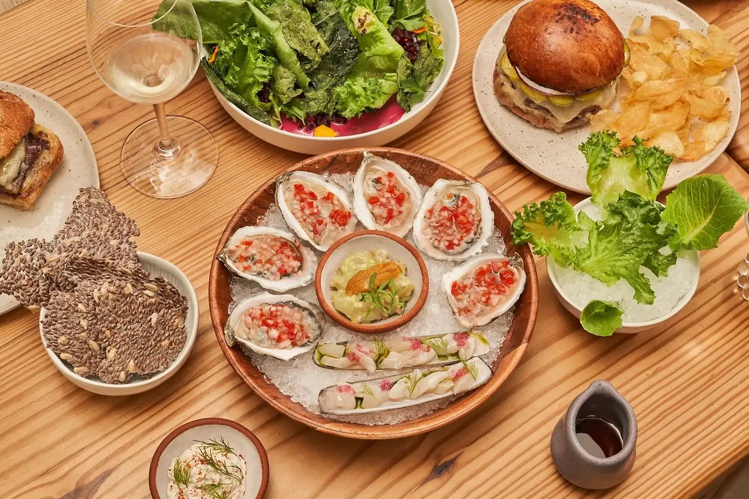 A table setting with raw oysters, salads, burgers, and sauces at Krüs Kitchen, bookable on OpenTable.